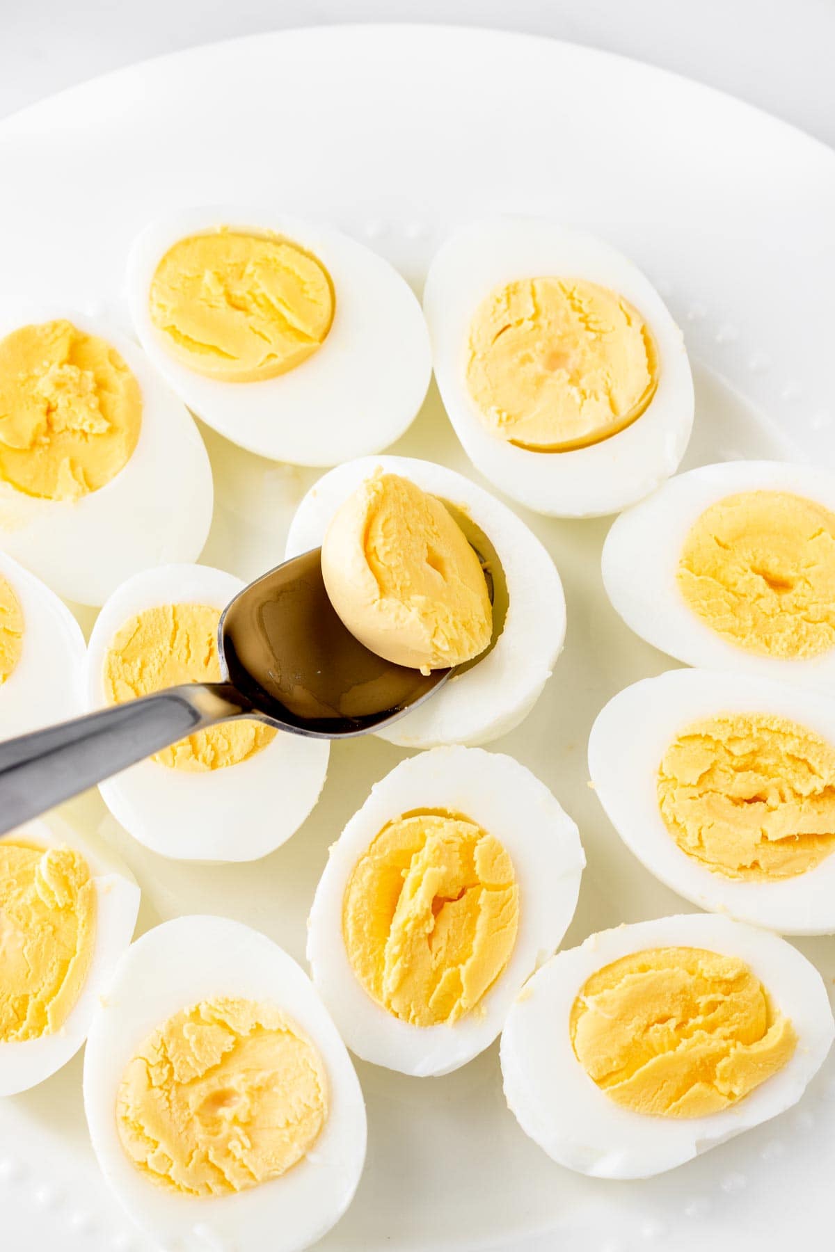 A spoon scooping out the yolks from halved egg whites.