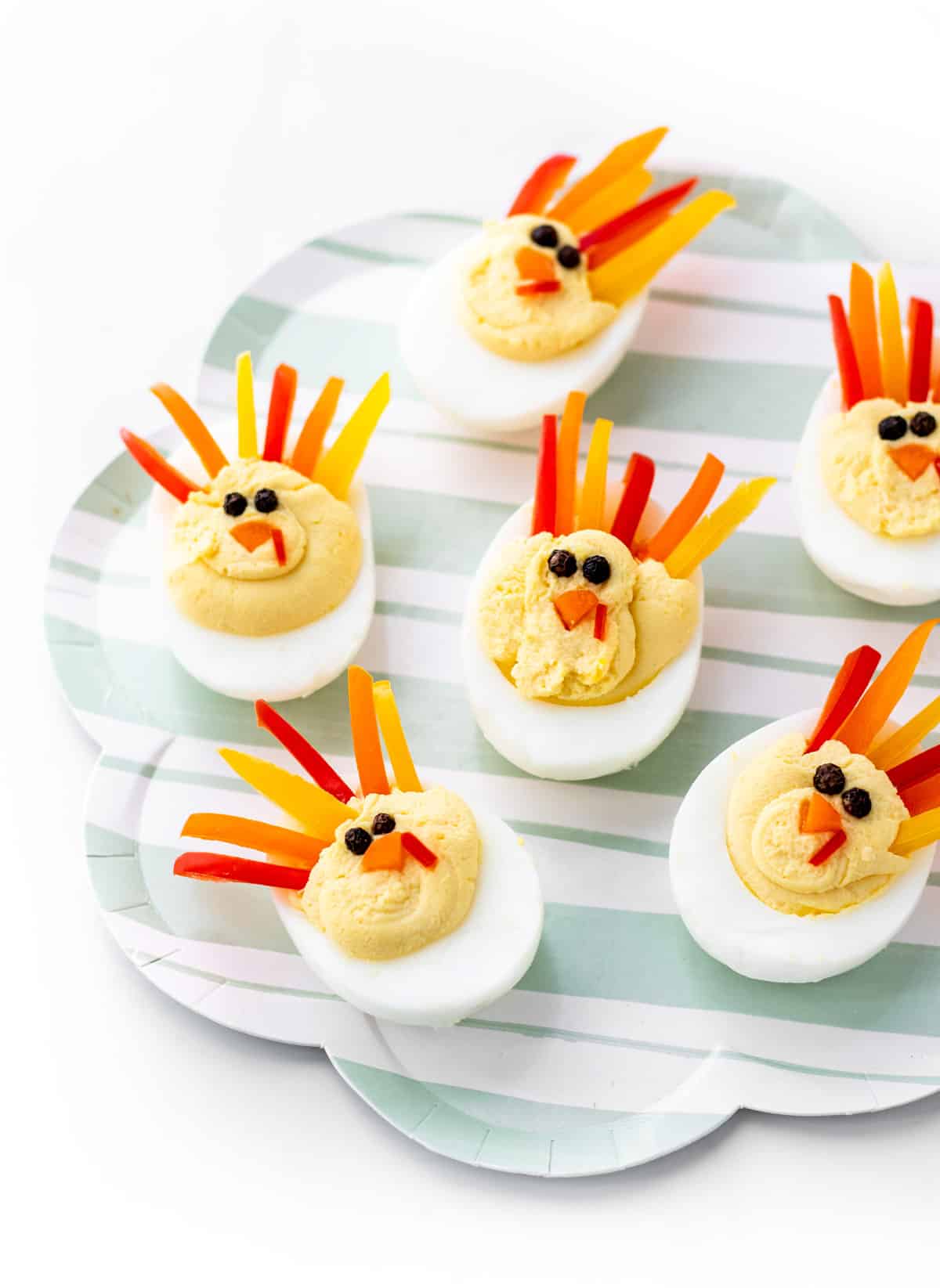 Turkey deviled eggs decorated with peppers, carrots and peppercorns on a plate.