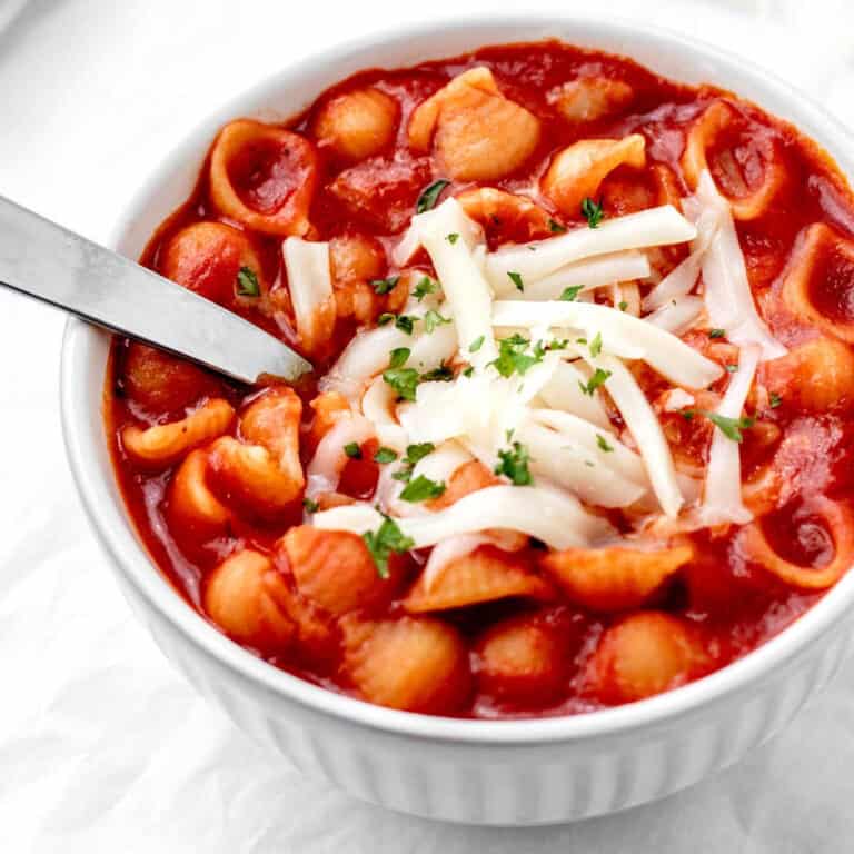 A bowl of seashell soup topped with cheese.