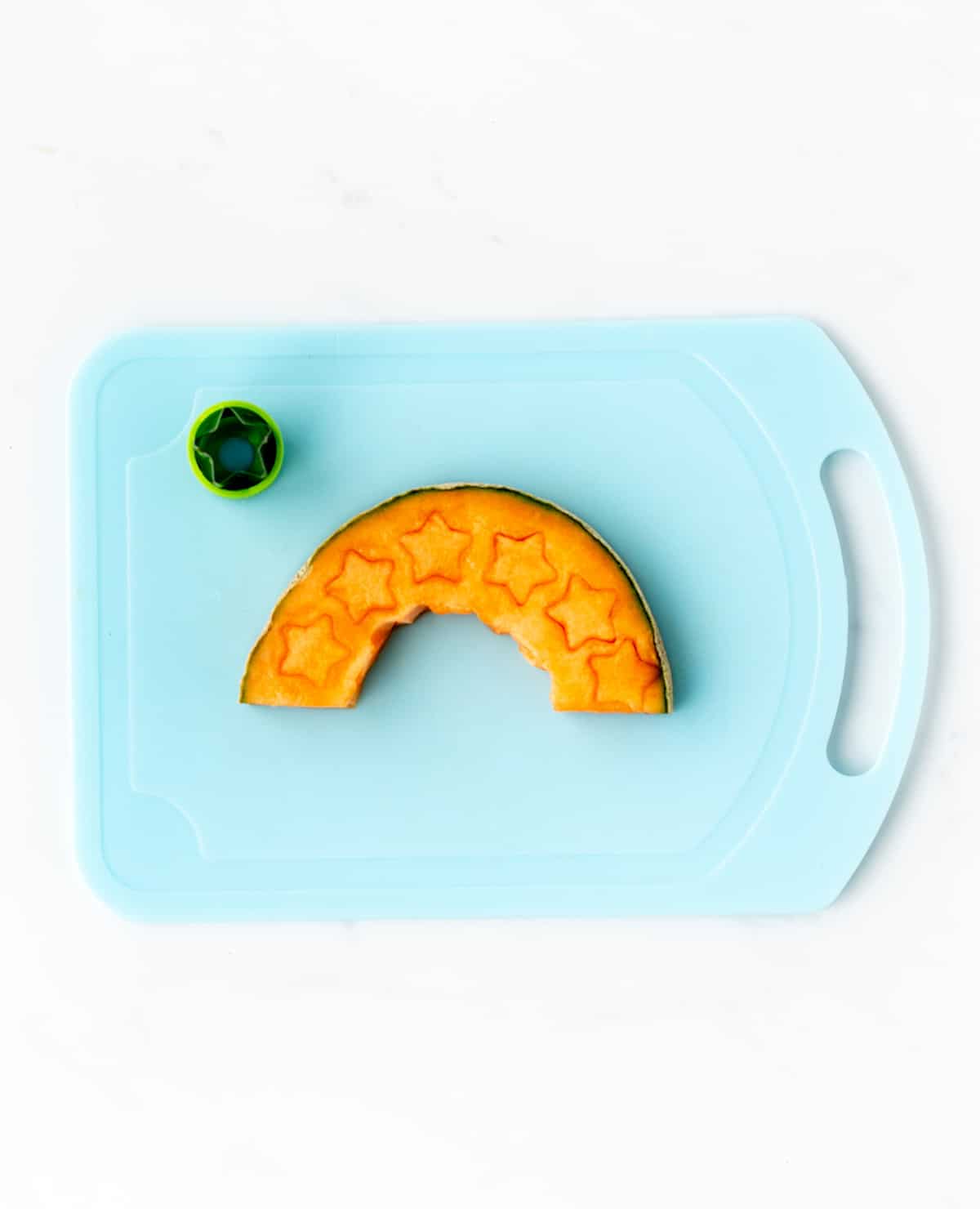 A piece of cantaloupe on a cutting board with small stars cut out with mini star cooking cutter.