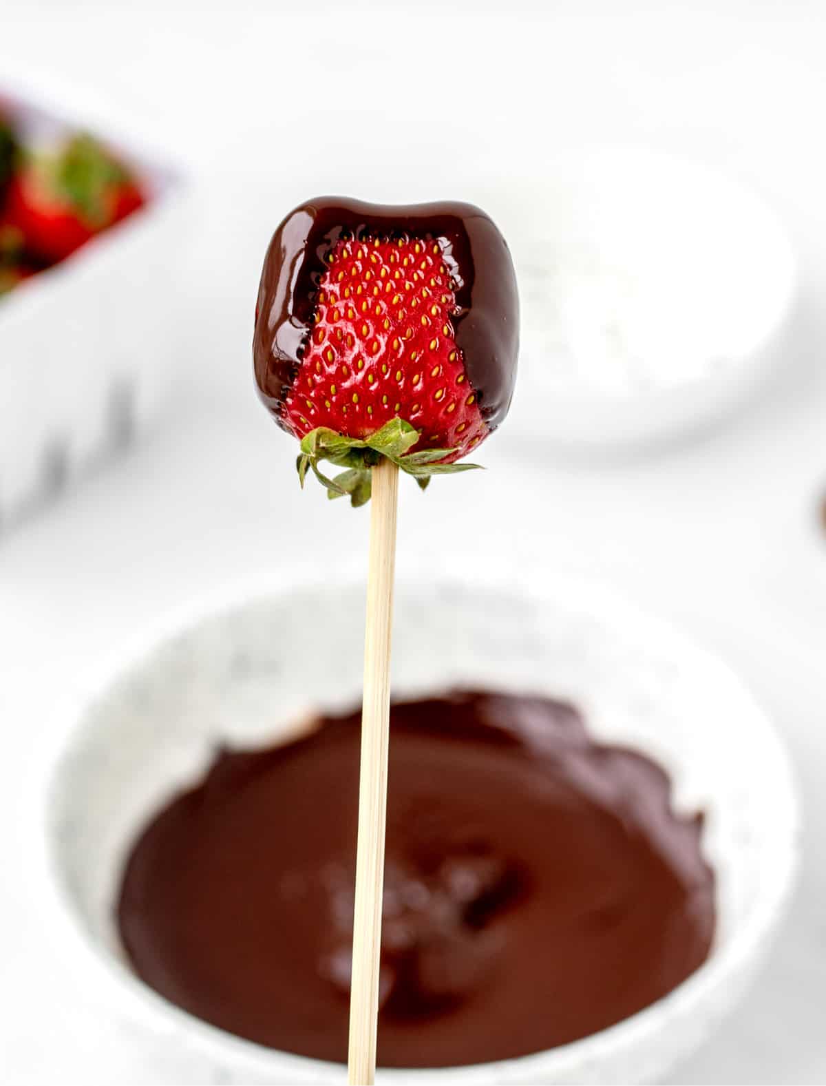 A chocolate covered strawberry with both sides covered in chocolate on a wooden skewer.