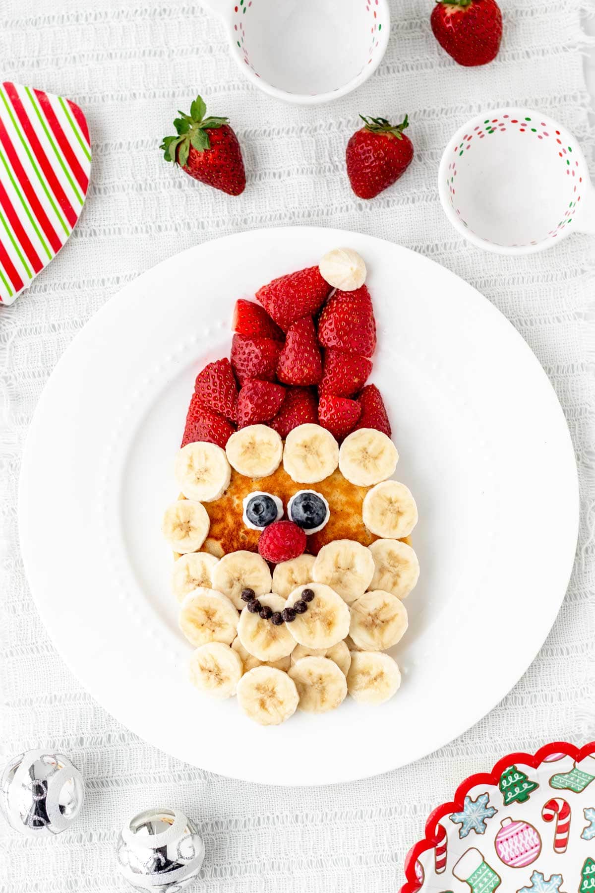 A birds-eye view of a Santa pancake with strawberries on a white plate.