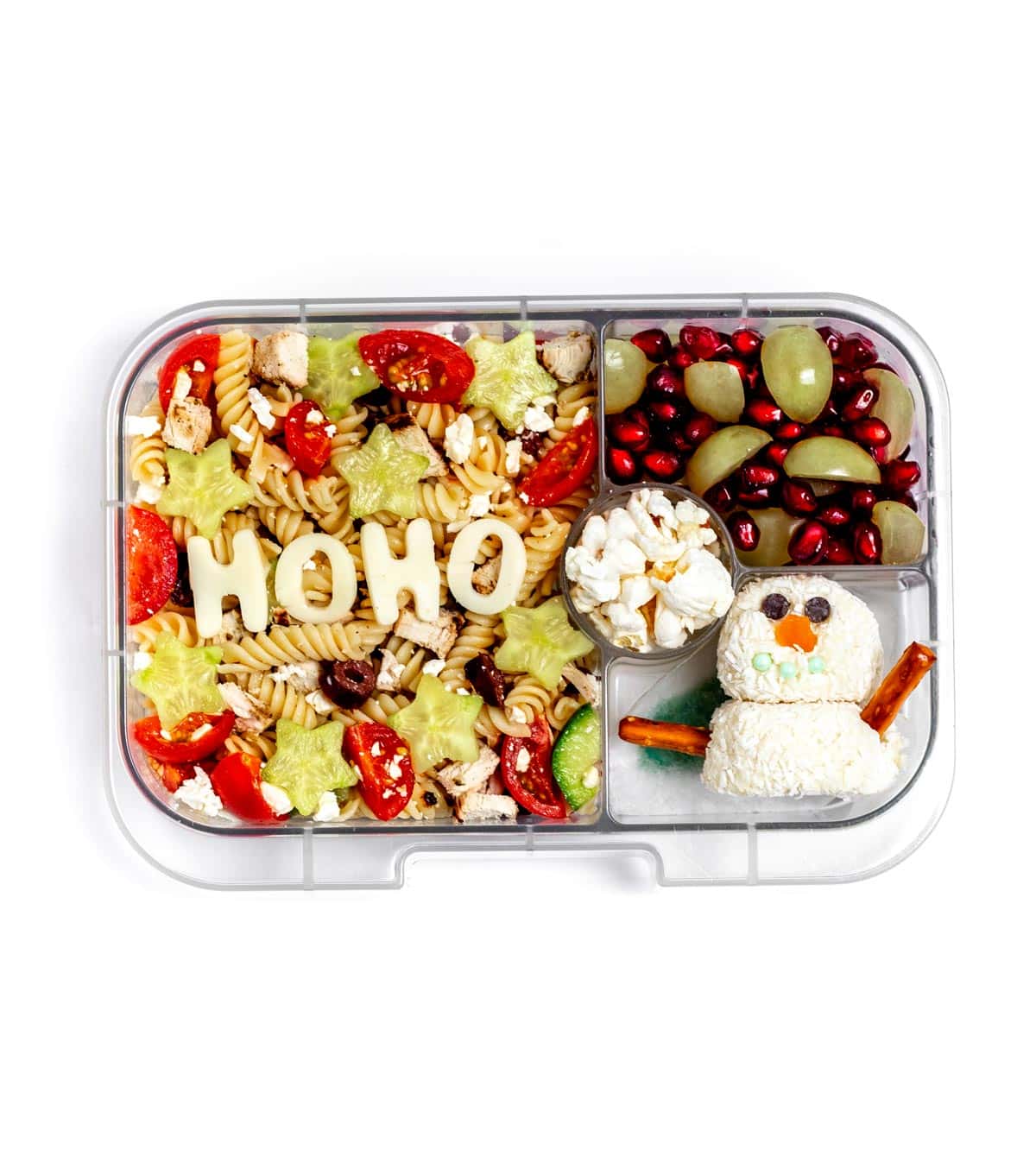 A lunchbox with Greek pasta salad, green grapes and pomegranate seeds, popcorn and a snowman truffle.