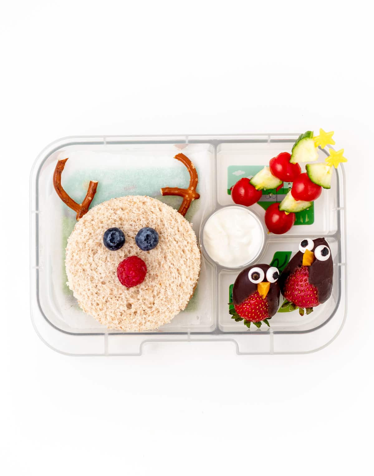 A lunchbox with a Rudolf sandwich, skewers of mini stars and cherry tomatoes, and two chocolate covered strawberry penguins.