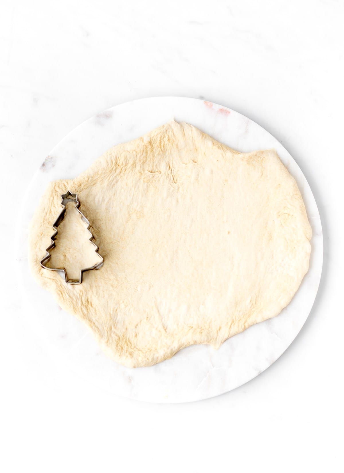 The Christmas tree cookie cutter being used to cut Christmas trees out of the dough.