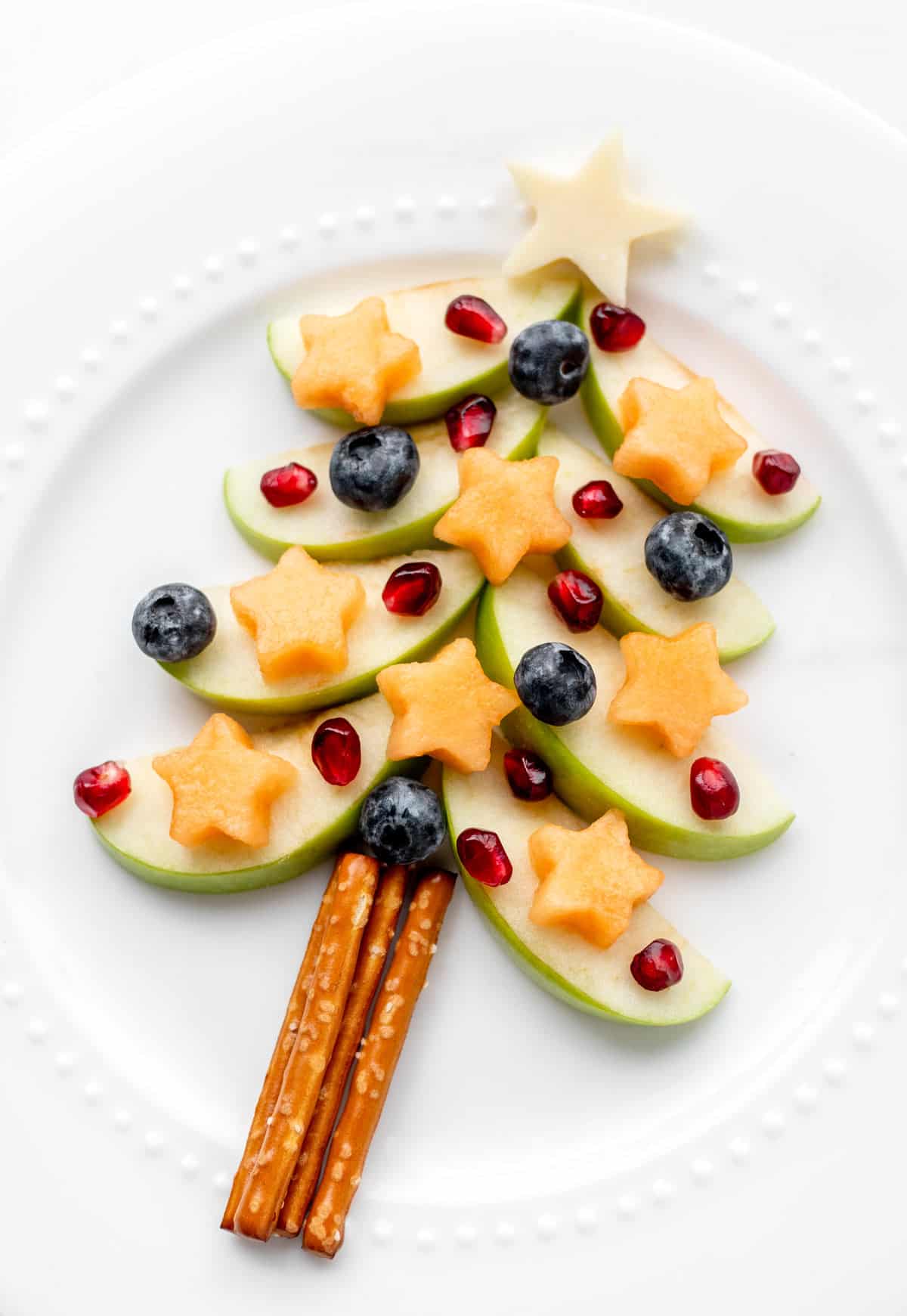 Apple Christmas tree made out of apples, pretzel sticks, cantaloupe stars, blueberries and pomegranate seeds.