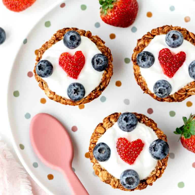 Three granola yogurt cups with berries on a polka dot plate.