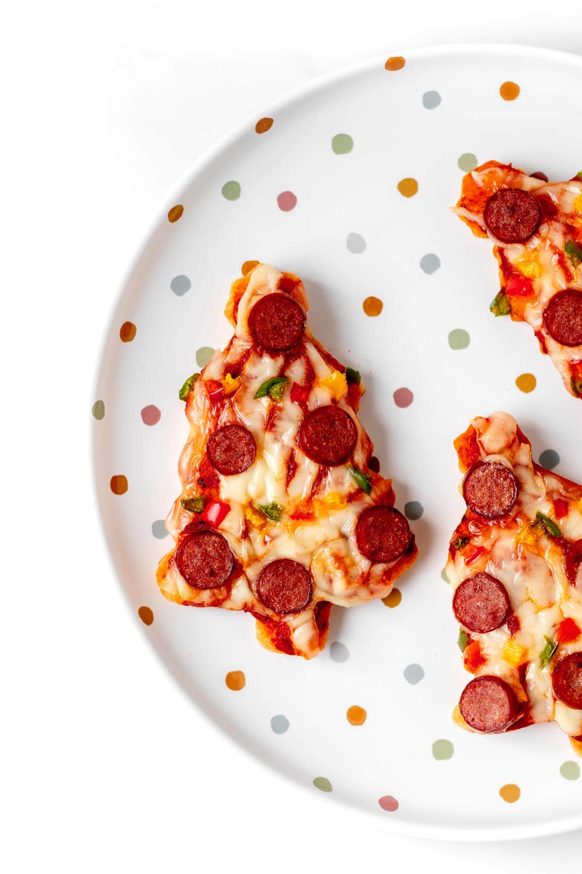 A close-up of the cooked and decorated mini Christmas tree pizzas on a decorative plate.