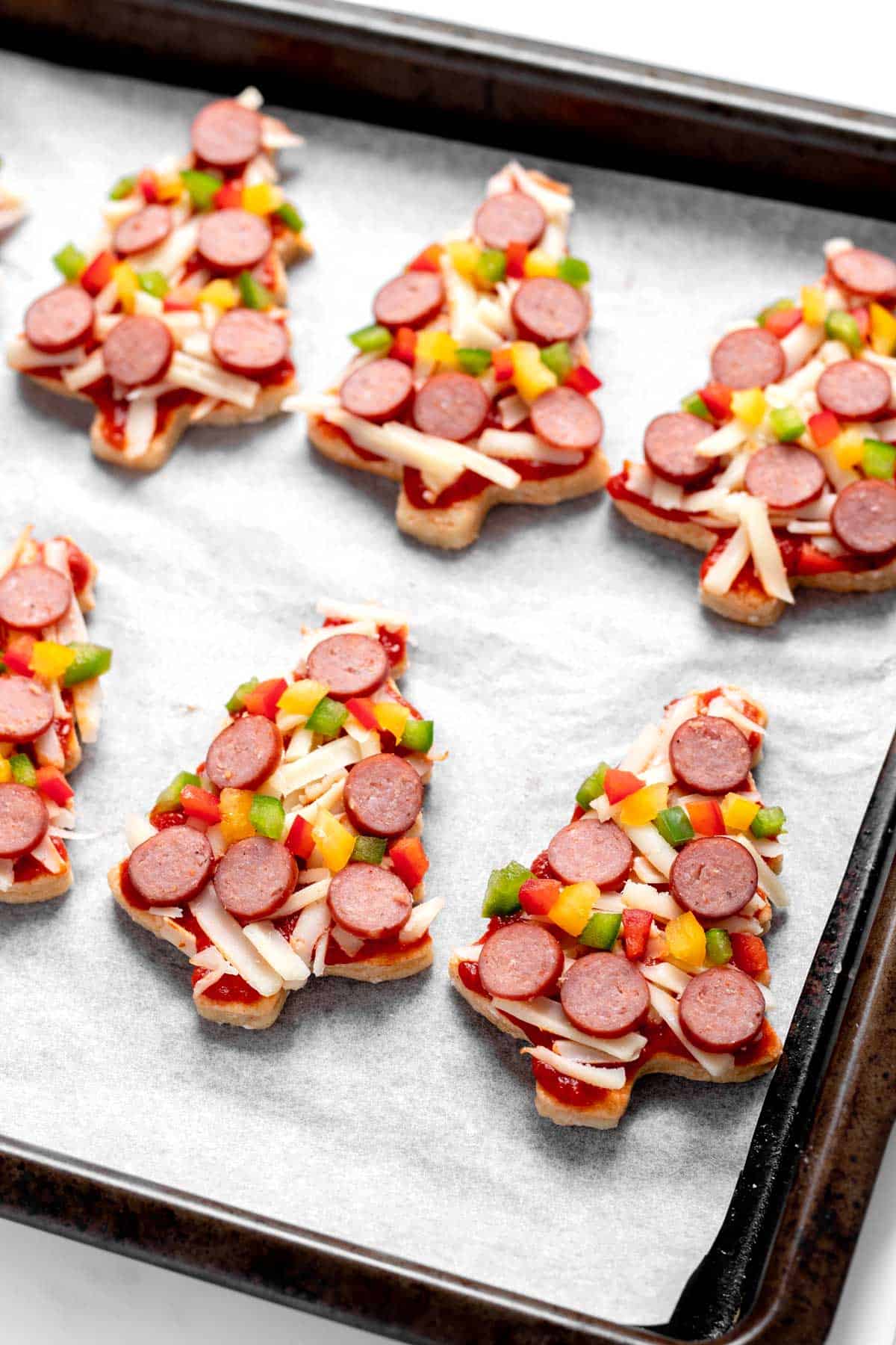 A close-up of the mini Christmas tree pizzas on a baking sheet prior to going in the oven.