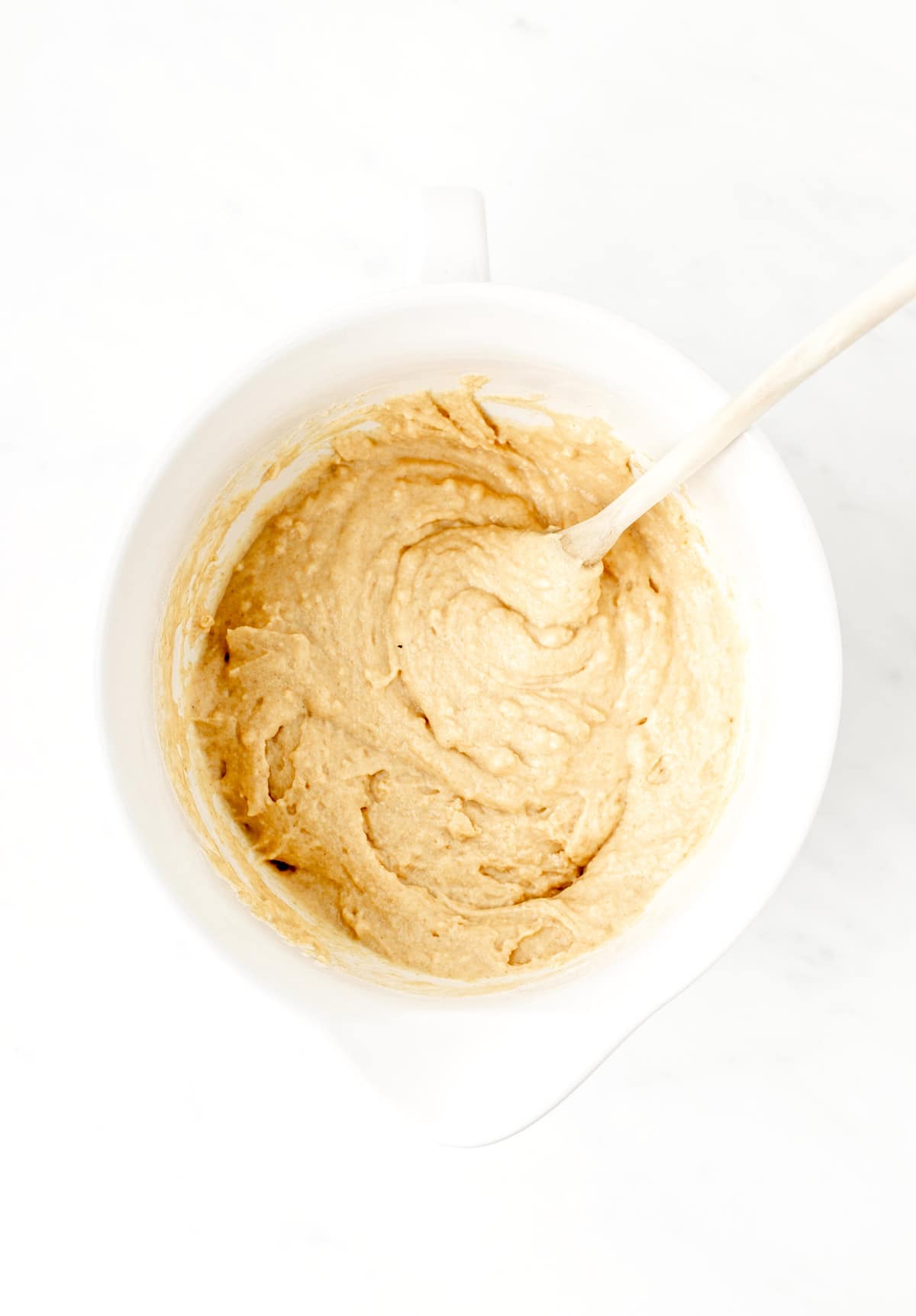 A wooden spoon mixing together the dry ingredients and the wet ingredients in a large bowl. 