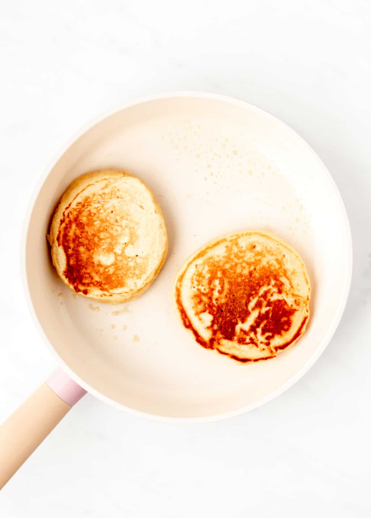 Two cooked pancakes in a frying pan.