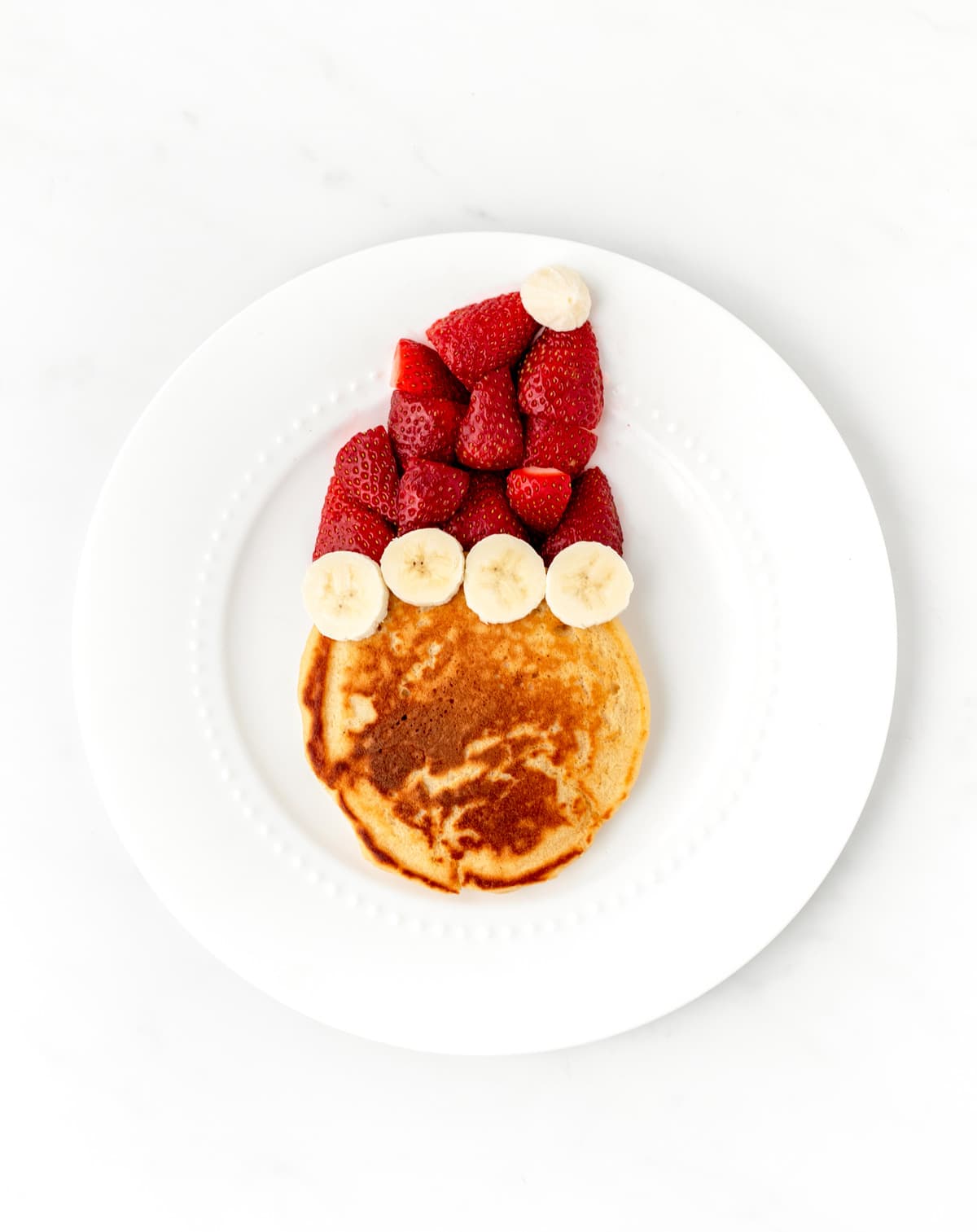 A pancake with a strawberry and banana Santa hat.