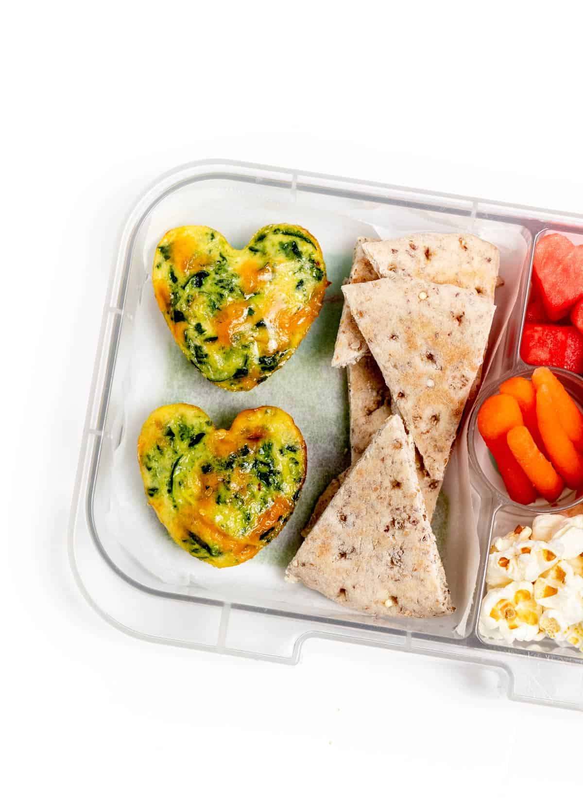 Zucchini egg muffins in a divided lunch box with triangle pitas and vegetables.