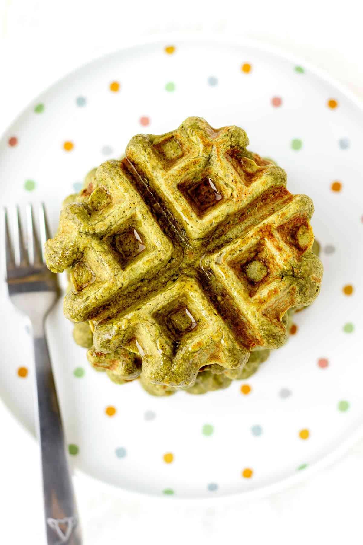 A spinach banana waffle on a polka dot plate next to a fork.