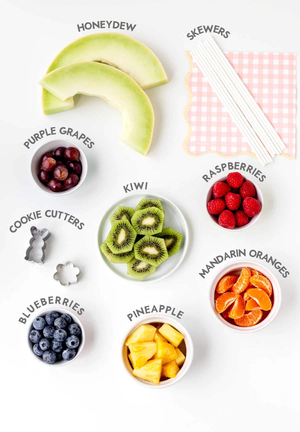 Individually portioned ingredients for the Easter fruit kabobs with text displaying what each one is.
