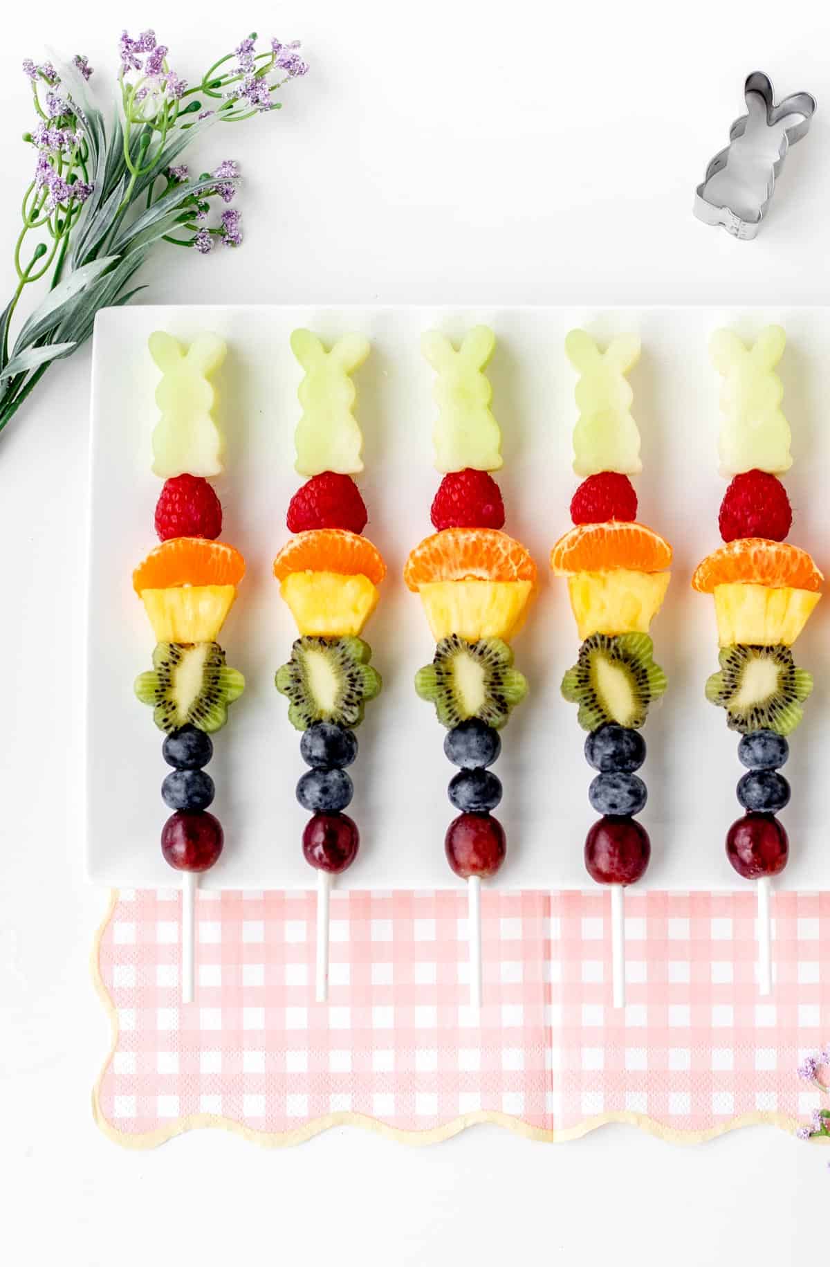 Easter fruit kabobs lined up on a white cutting board.