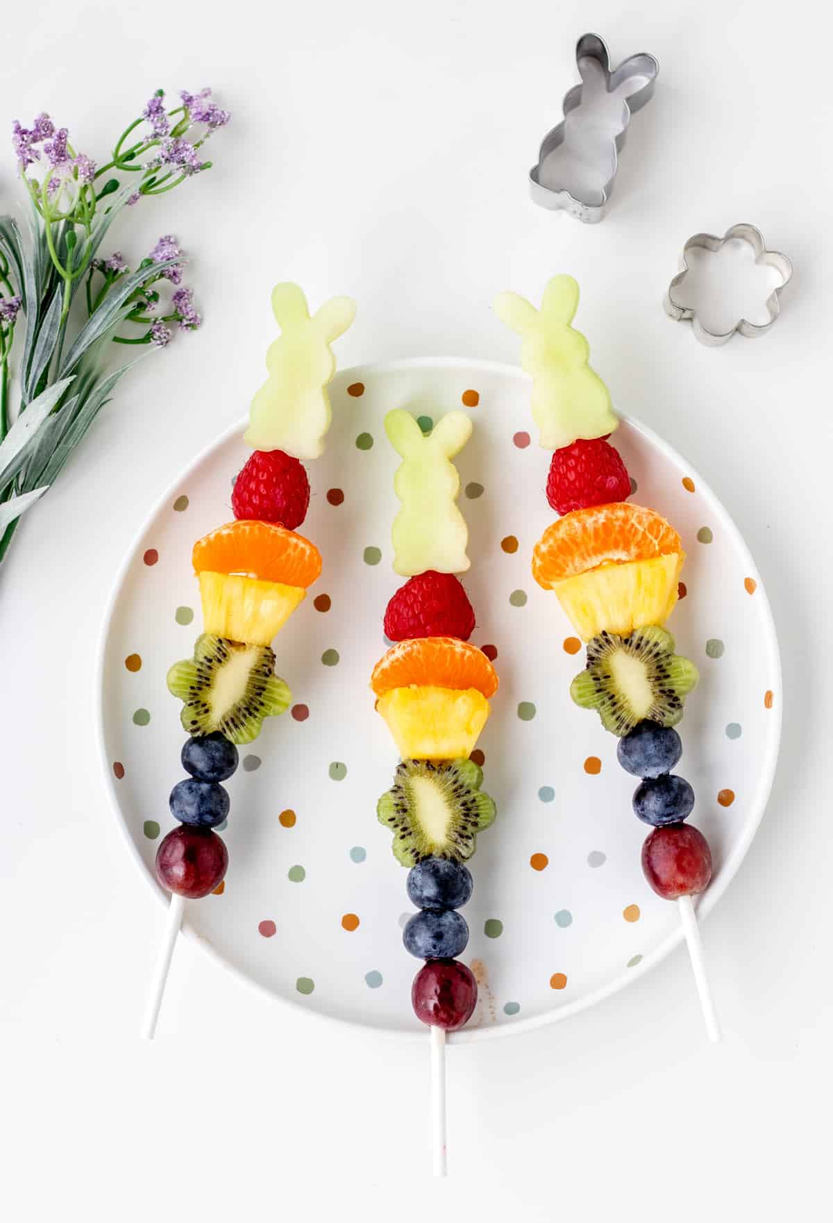 3 Easter fruit kabobs on a white polka-dotted plate.