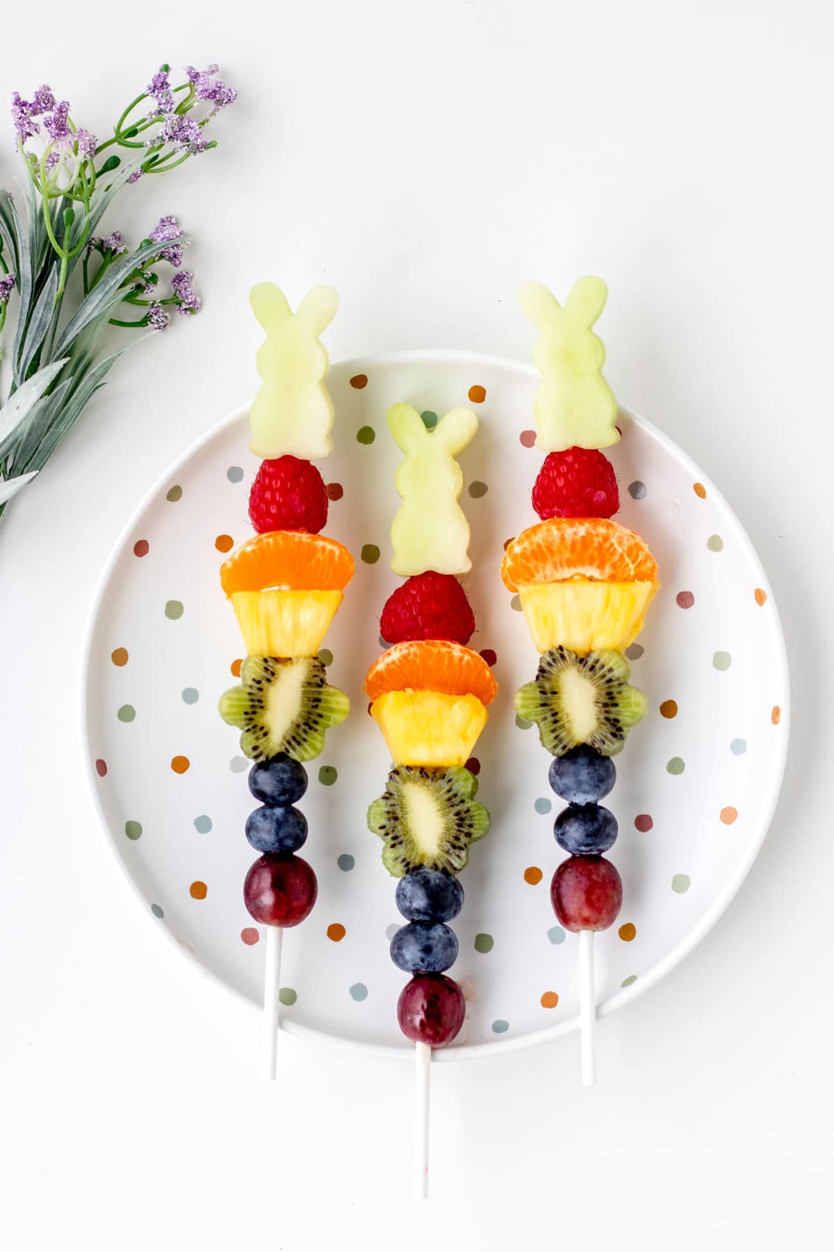 Easter fruit kabobs lined up on a circular, white polka-dotted plate.