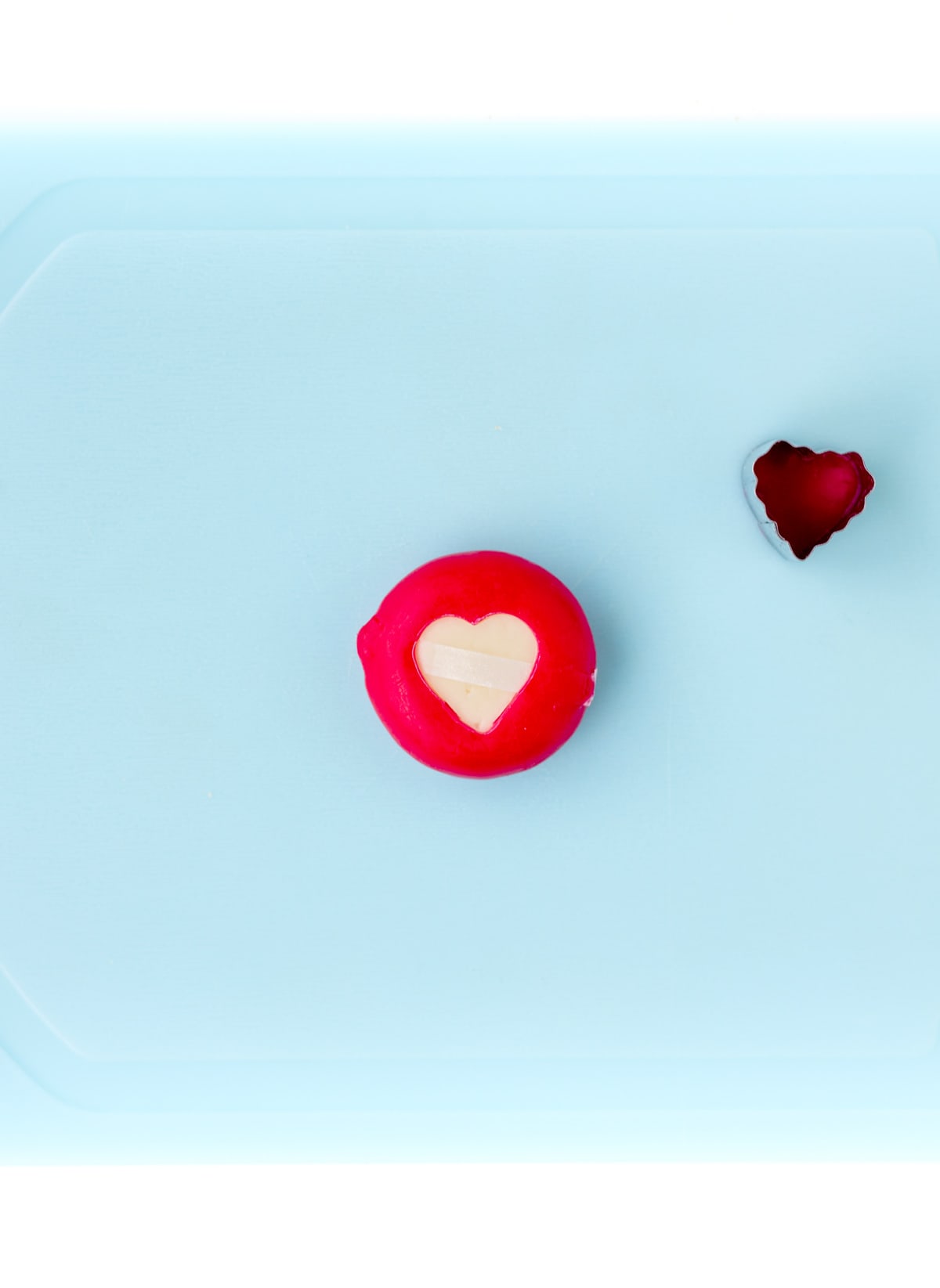 Cutting a heart out of the wax on the baby bel cheese using a small heart shaped cookie cutter.