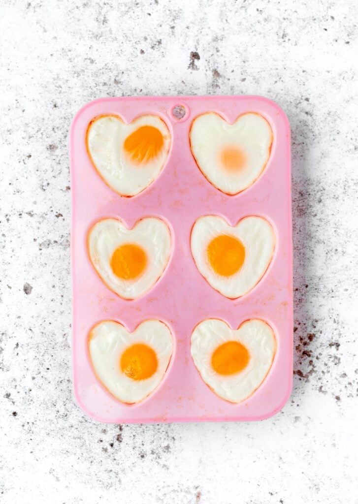 6 heart shaped eggs in a muffin pan after baking.