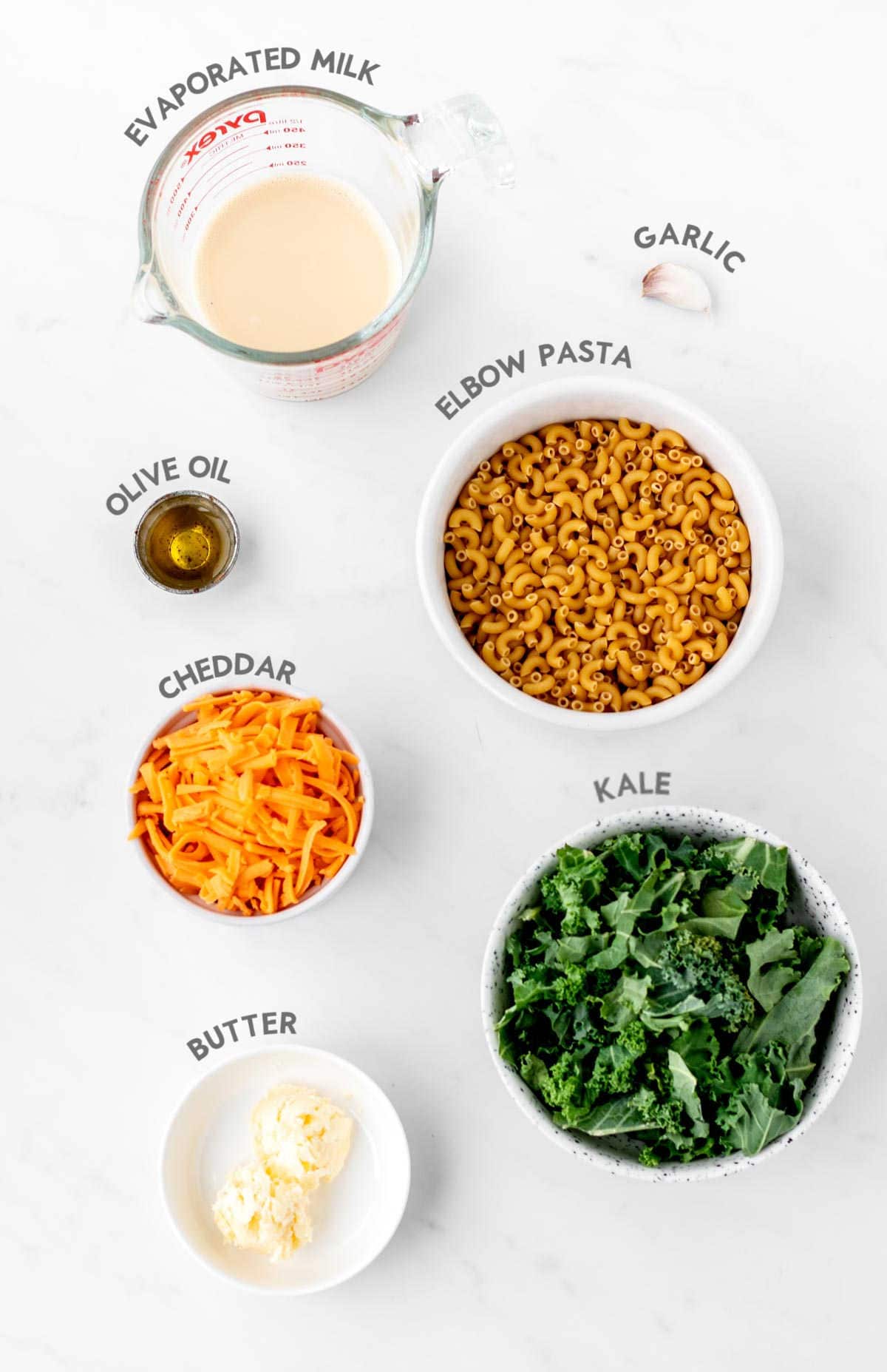 Individually portioned ingredients for the kale mac and cheese with text labeling each ingredient.