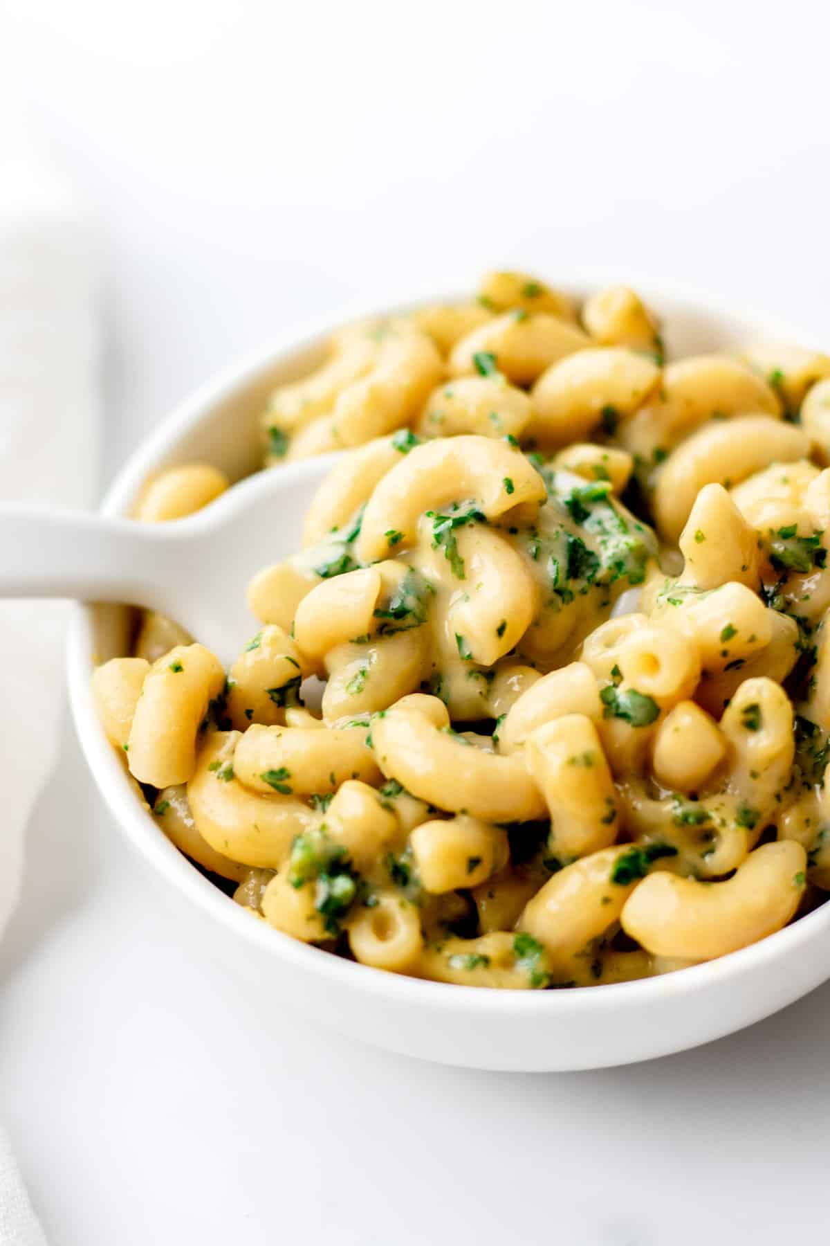 Kale mac and cheese in a small white bowl with a white spoon in it.