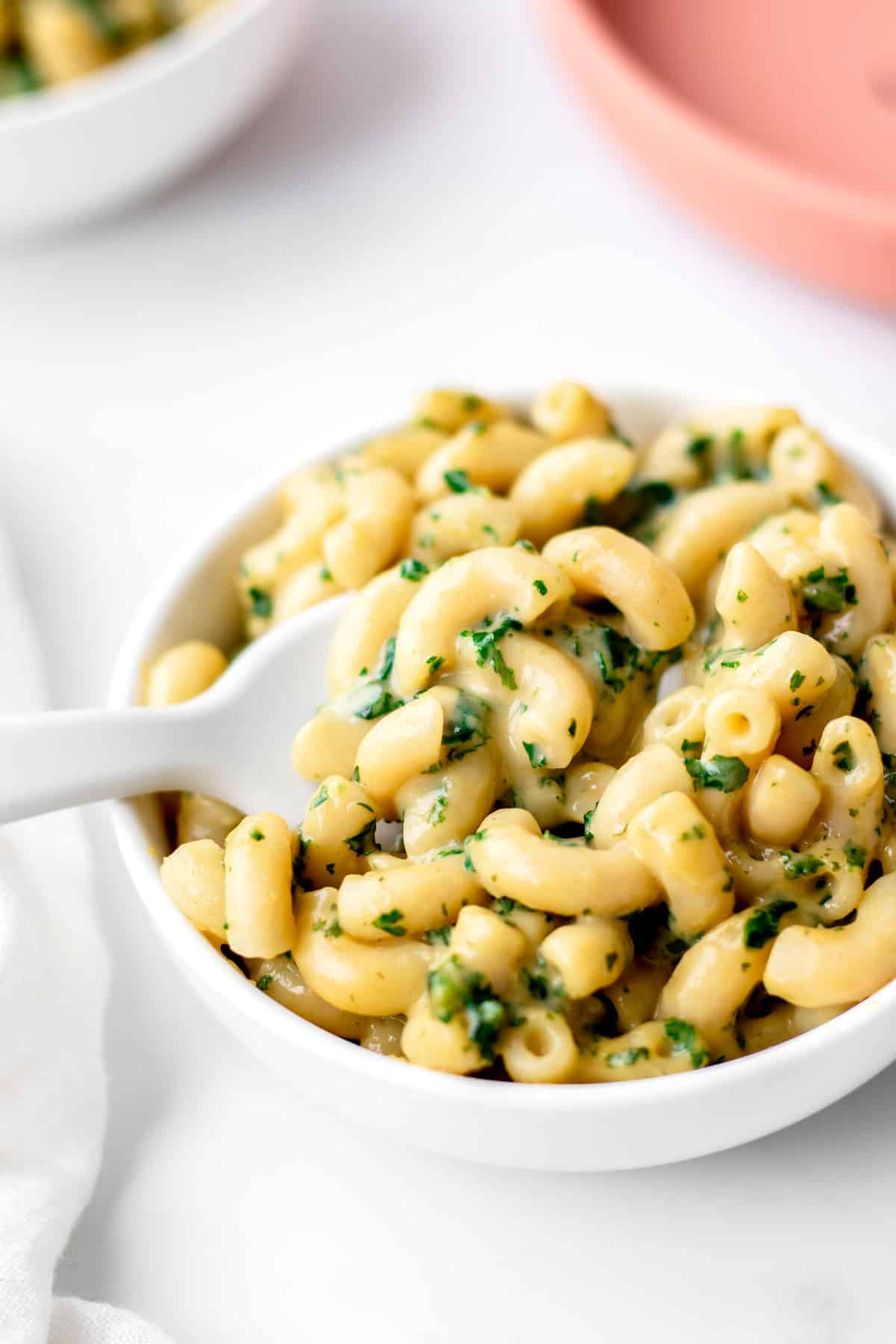 Kale mac and cheese in a white bowl with a white spoon in it.