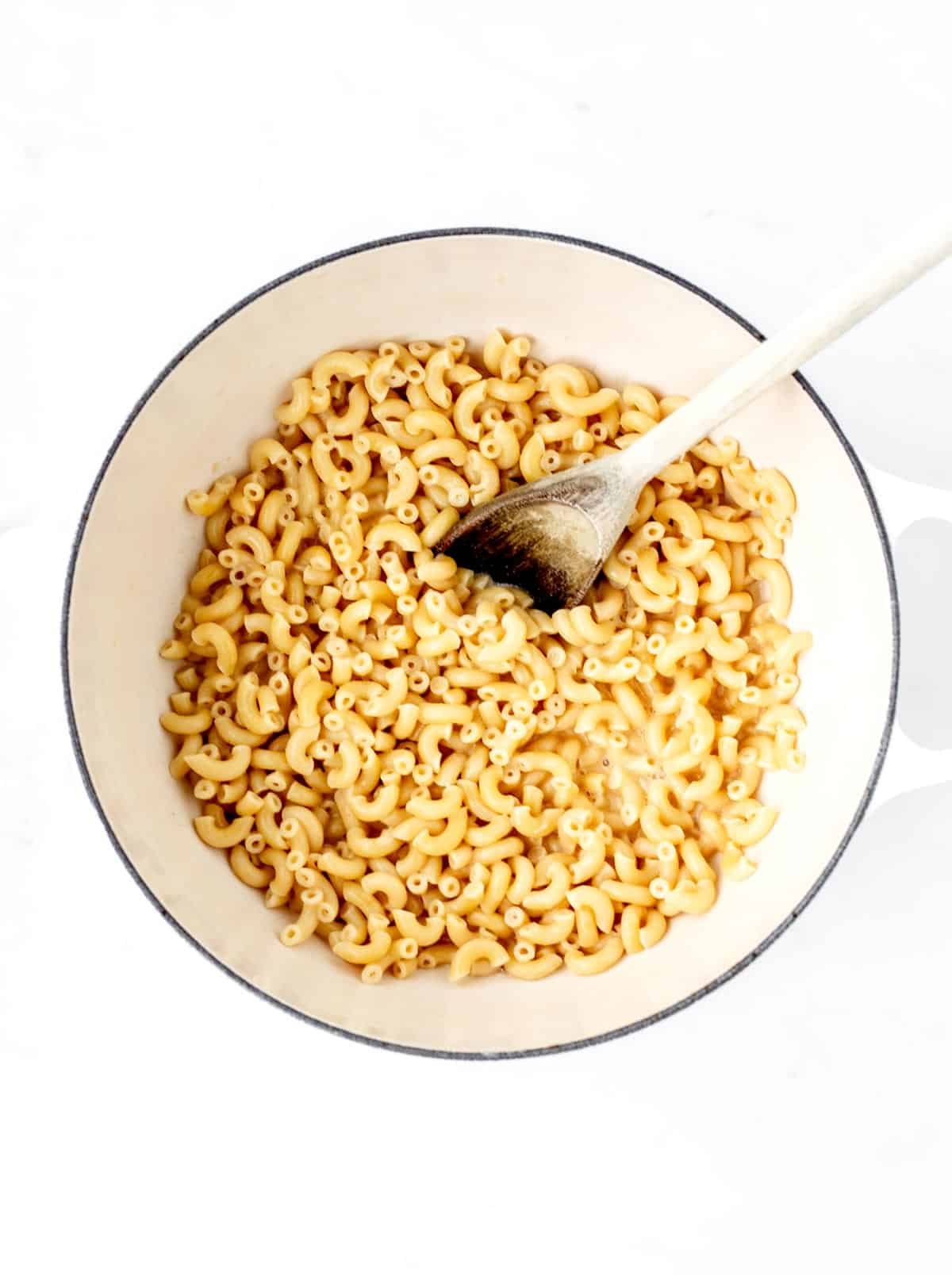 Incorporating the cooked pasta into the sauce with a wooden spoon.