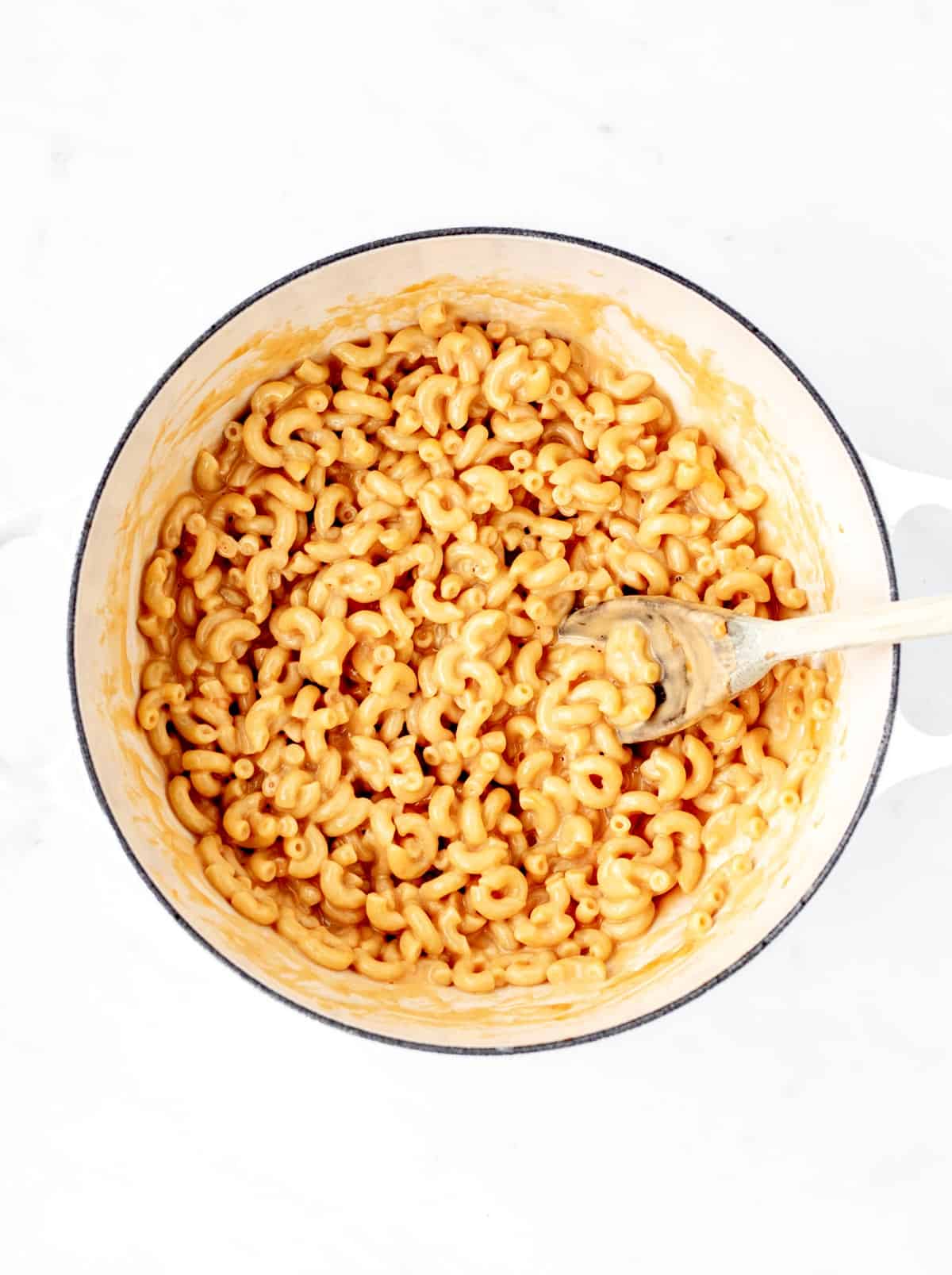 The cooked pasta being mixed with the sauce in a large pot with a spoon.