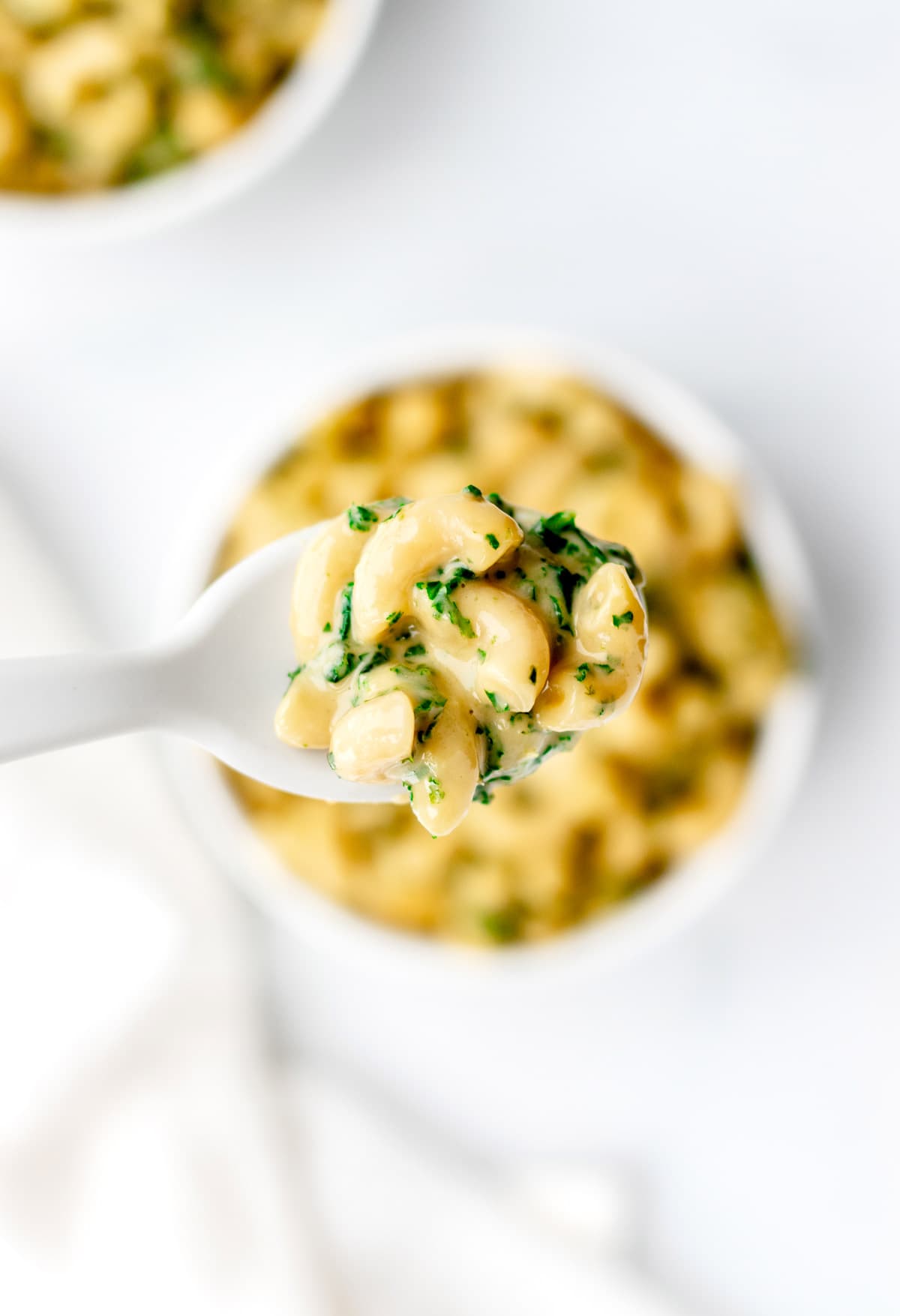 A close-up of a spoonful of the kale mac and cheese with a bowl of it in the background.