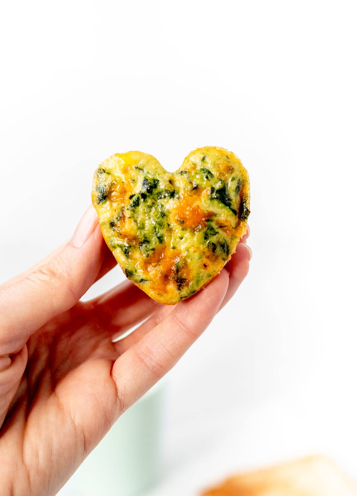 A mini zucchini frittata muffin in the shape of a heart being held in someone's hand.