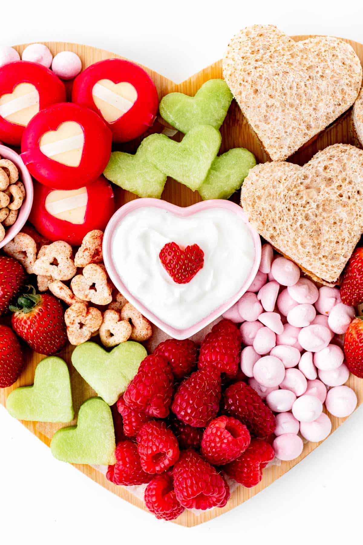 A close-up of the center of the heart shaped charcuterie board displaying the yogurt with heart shaped strawberry on top surrounded by other snacks.