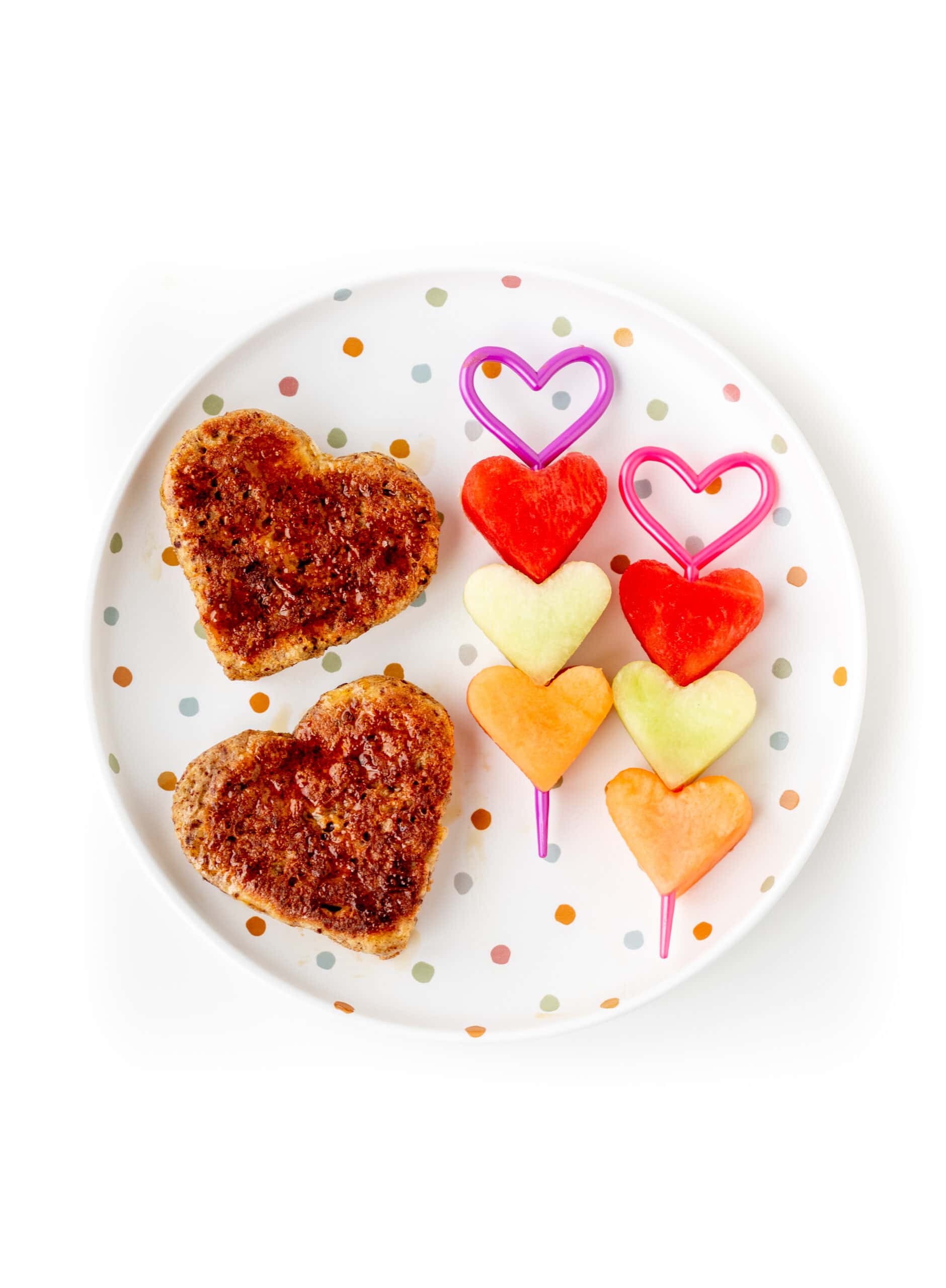 Heart French toast and heart fruit kabobs on a polka dot plate.