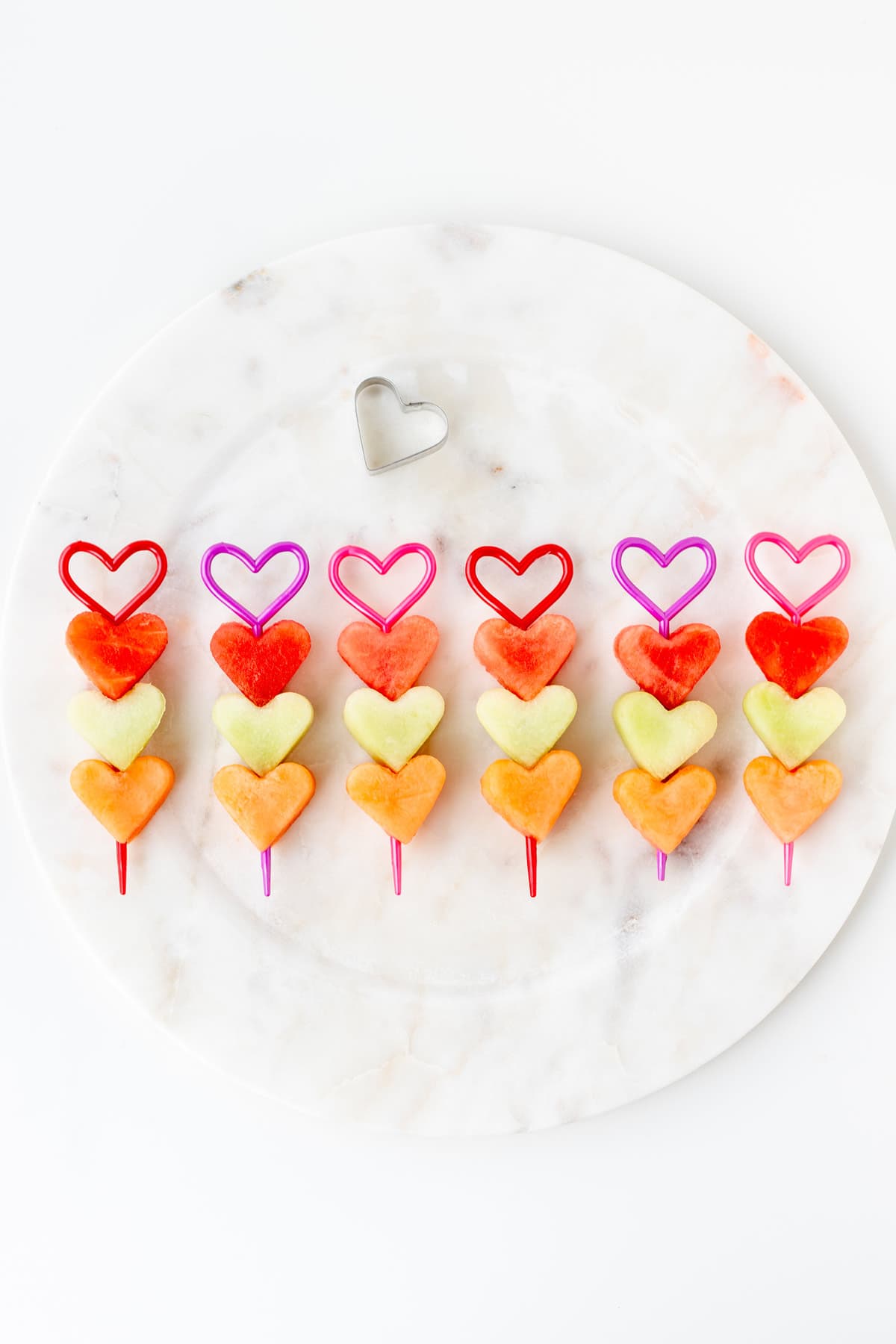 Valentine's Day fruit kabobs lined up on a decorative plate.