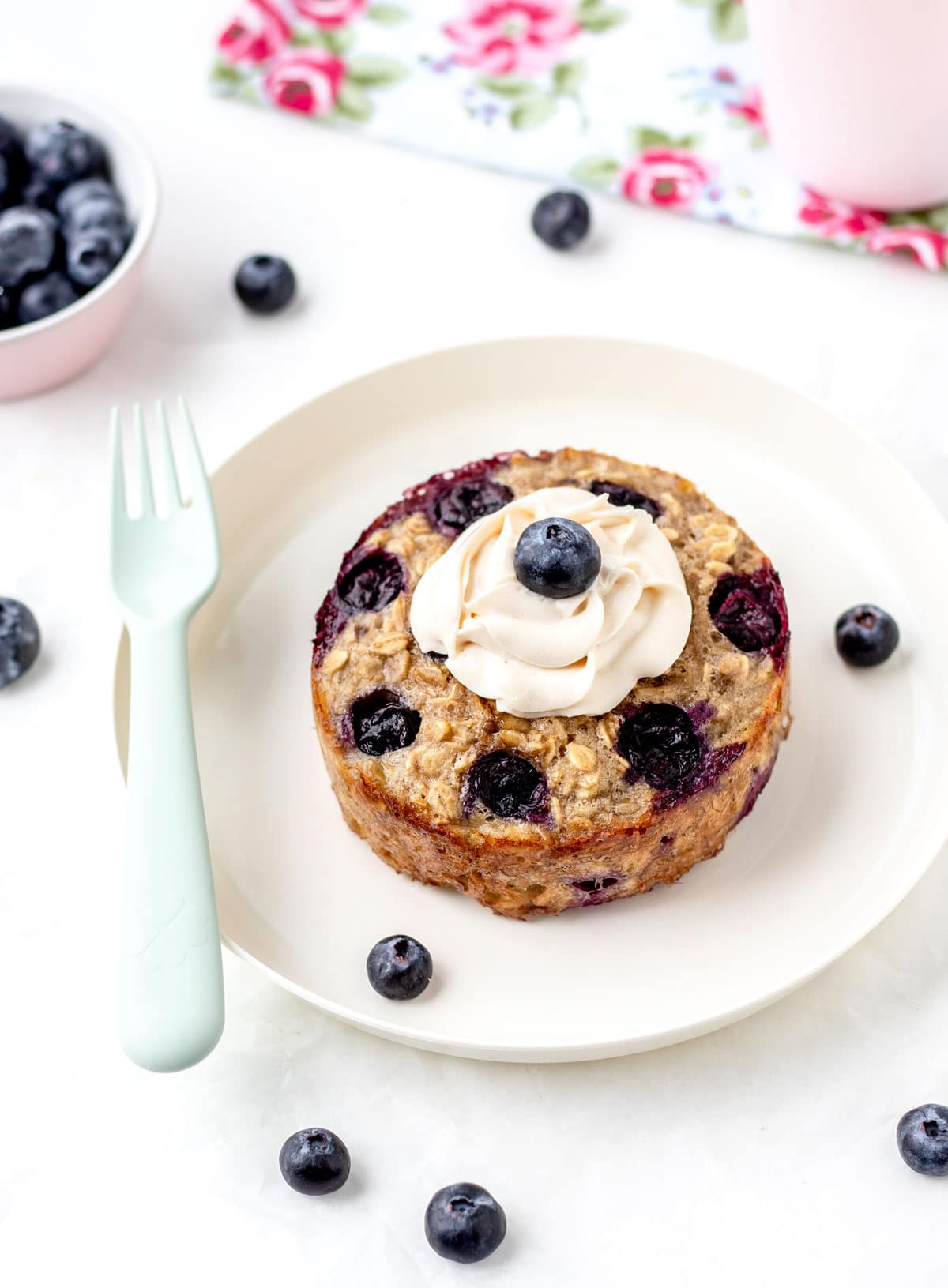 Baked oats for one on a white plate with a dollop of yogurt and a blueberry on top.