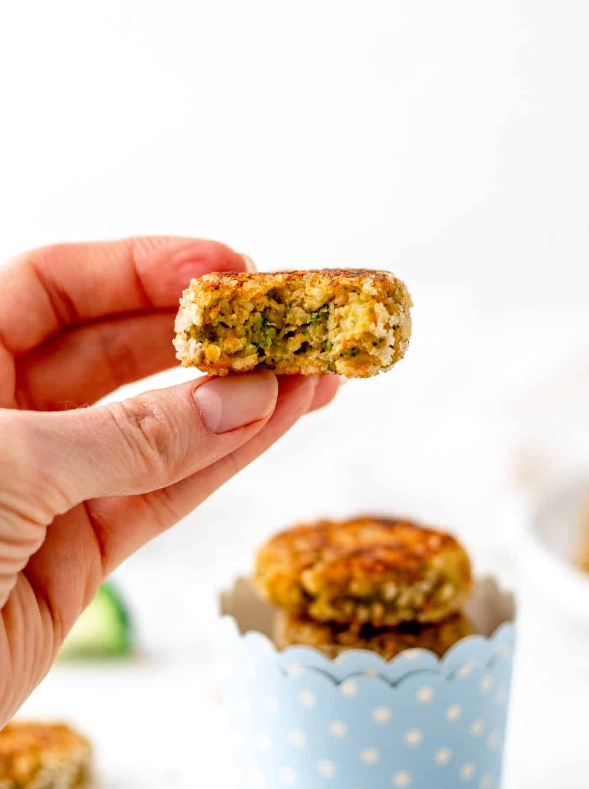 A chickpea veggie nugget in someone's hand with a bowl of stacked veggie nuggets in the background.