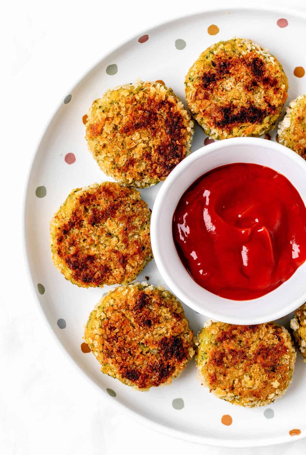 Chickpea veggie patties forming a circle around a bowl of ketchup on a polka dotted plate.