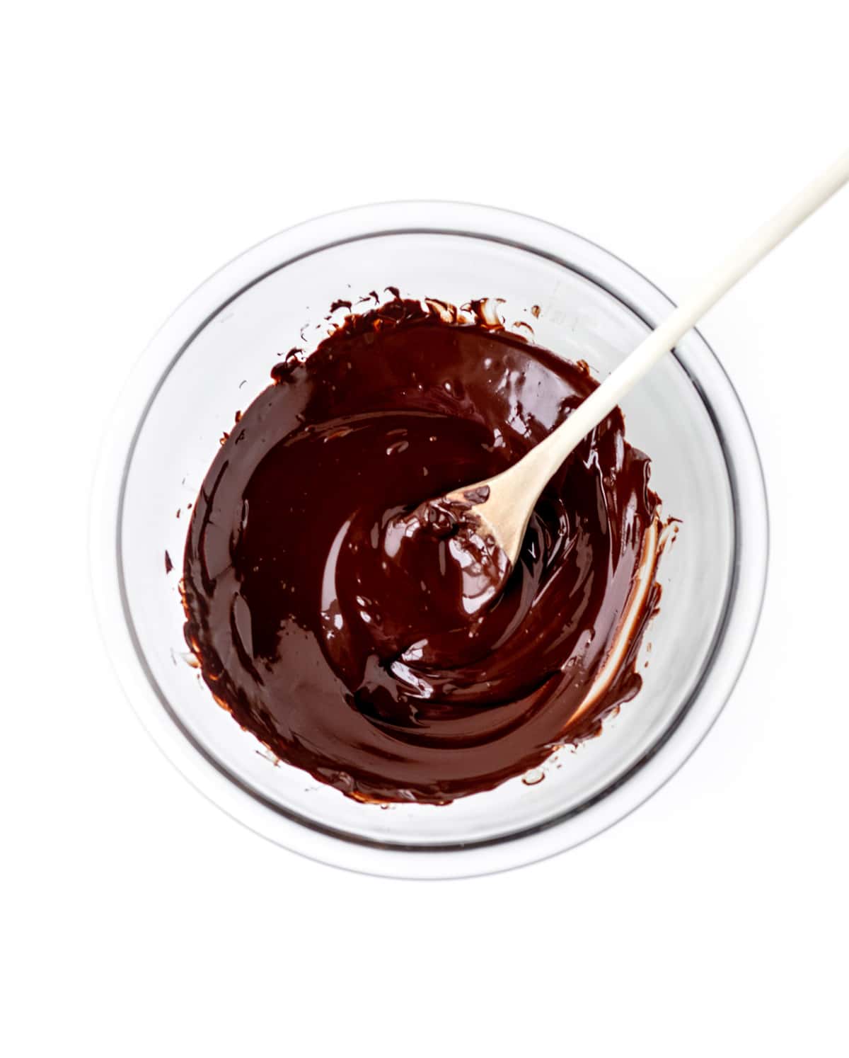 A glass bowl of melted chocolate and a wooden spoon.