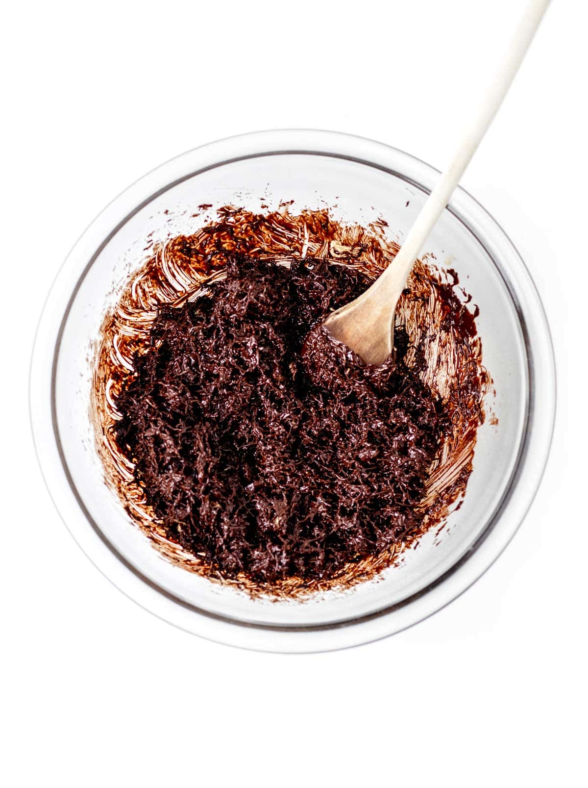 Mixing the chocolate chips and shredded wheat in a glass bowl with a wooden spoon.