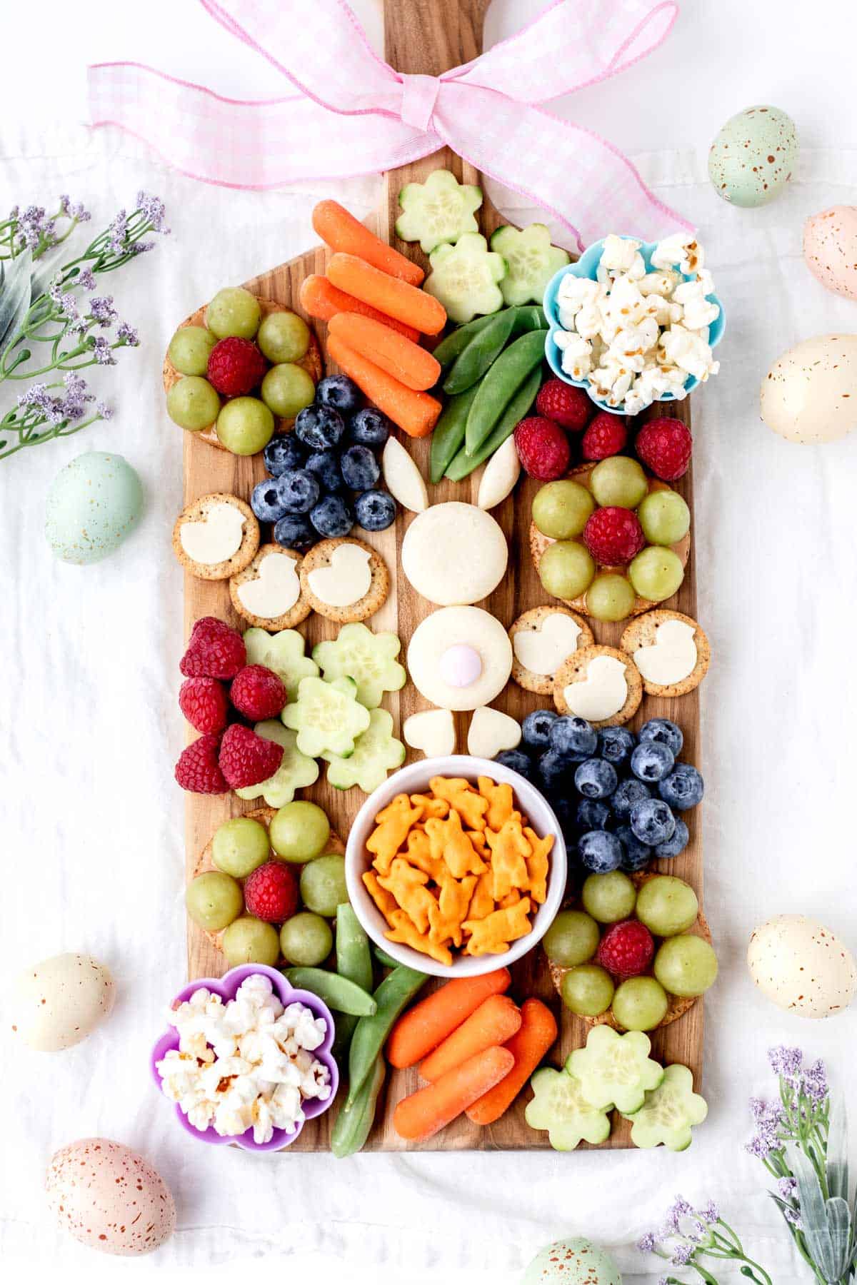 A fully assembled Easter bunny snack board on a counter, with pastel colored eggs surrounding it.