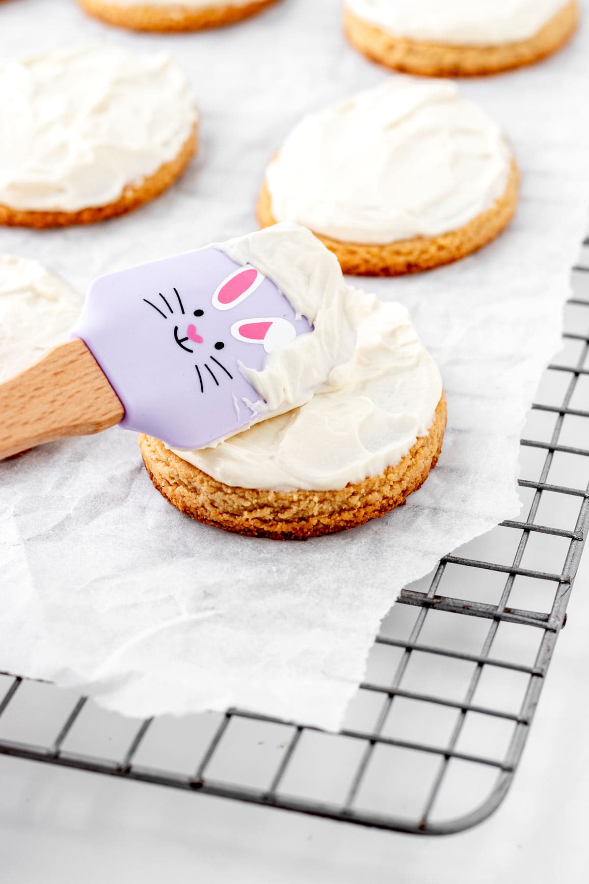 Spreading the cream cheese frosting onto the cookies with a spatula.