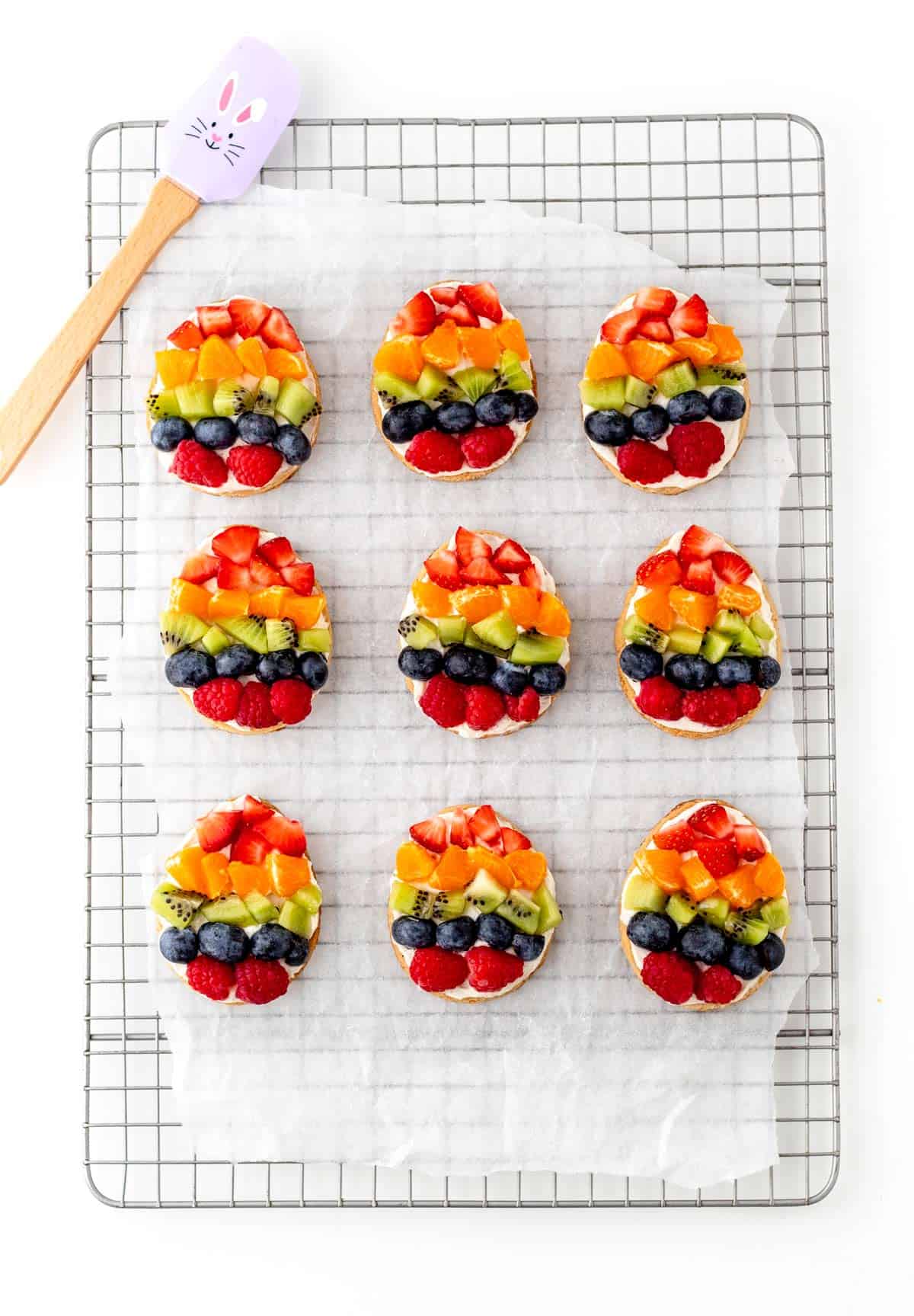 Mini Easter fruit pizza cookies on a cooling rack lined with parchment paper.