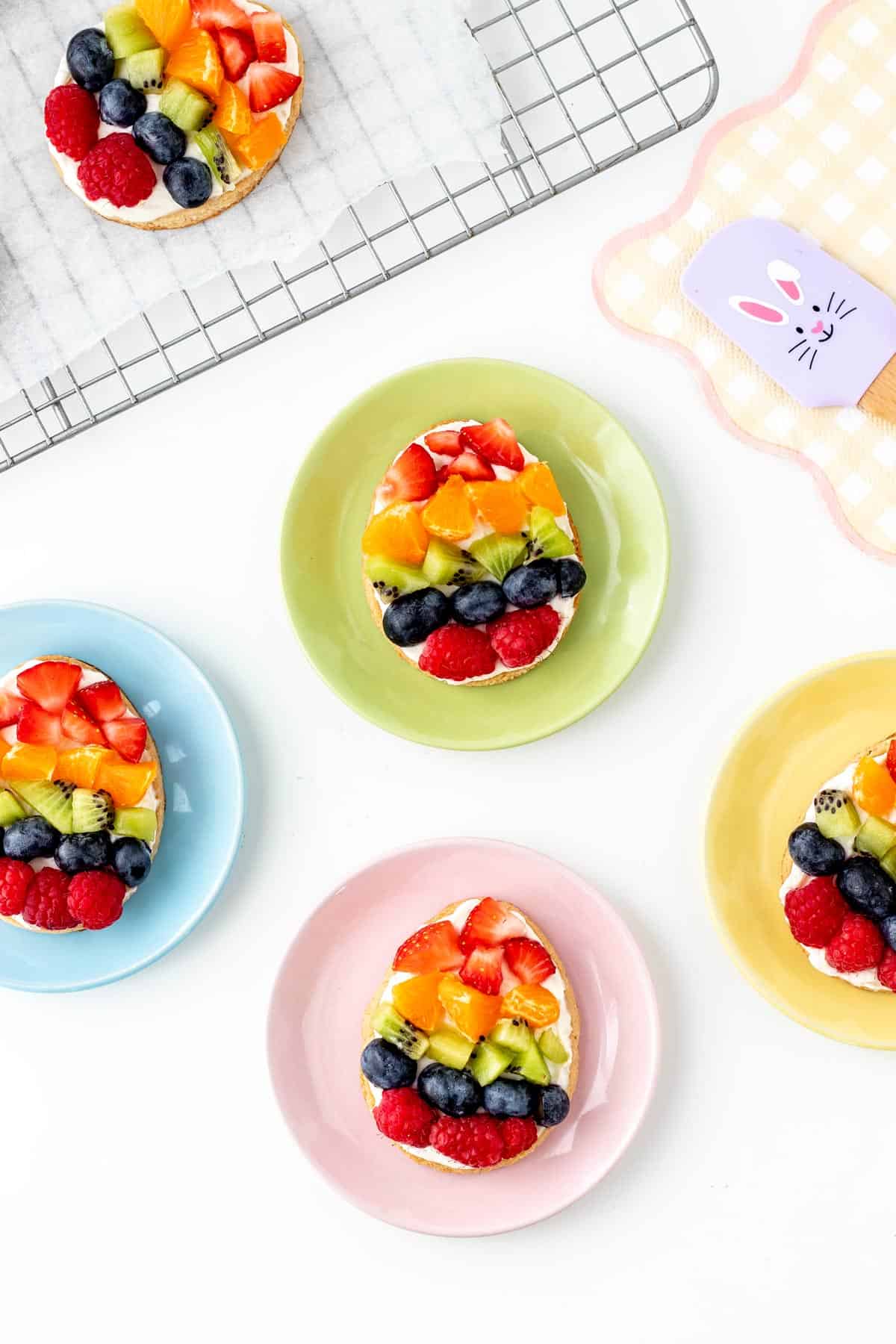 Decorated mini Easter fruit pizza cookies on small plates of different colors.