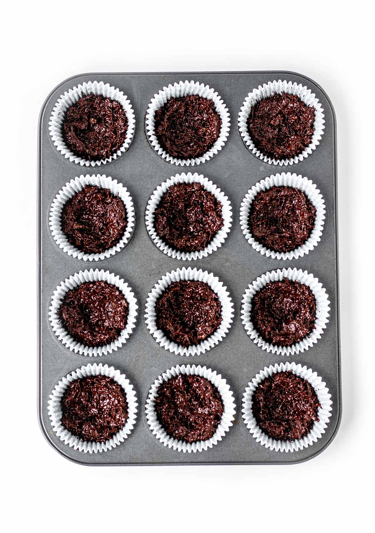 Chocolate shredded wheat Easter nests pressed into paper liners in a muffin pan, prior to adding the chocolate eggs.