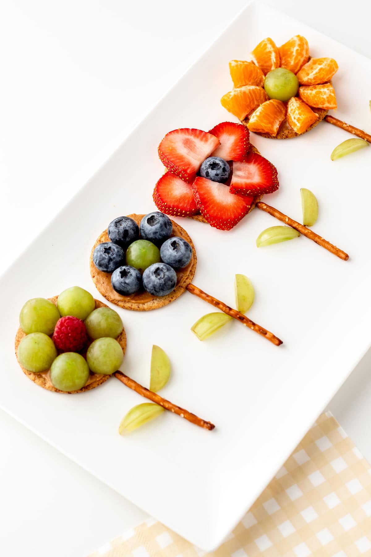 A close-up of edible flower crackers made of fruit and pretzel sticks on a white platter.