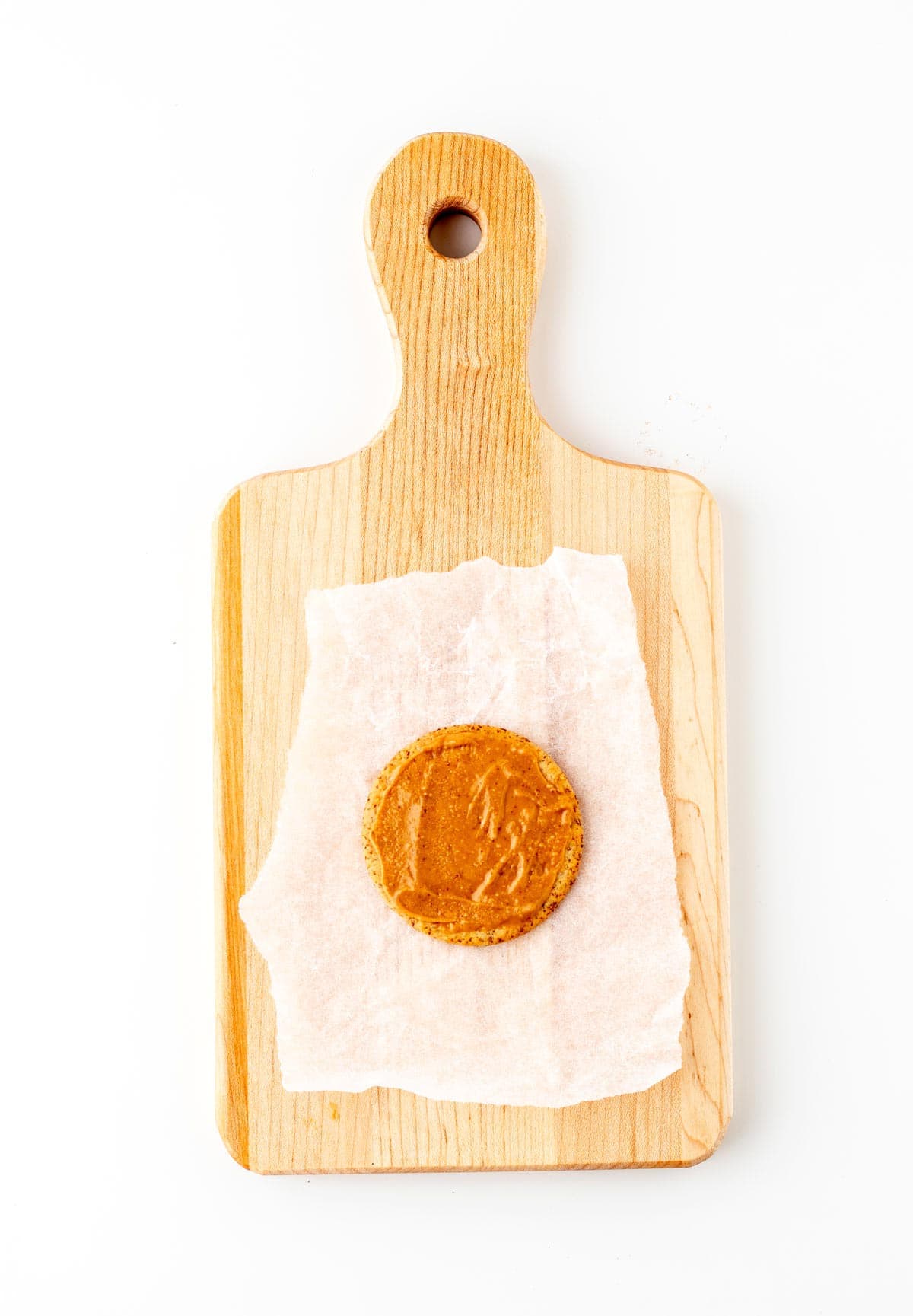 A single cracker with a thin layer of peanut butter spread on it on a cutting board.