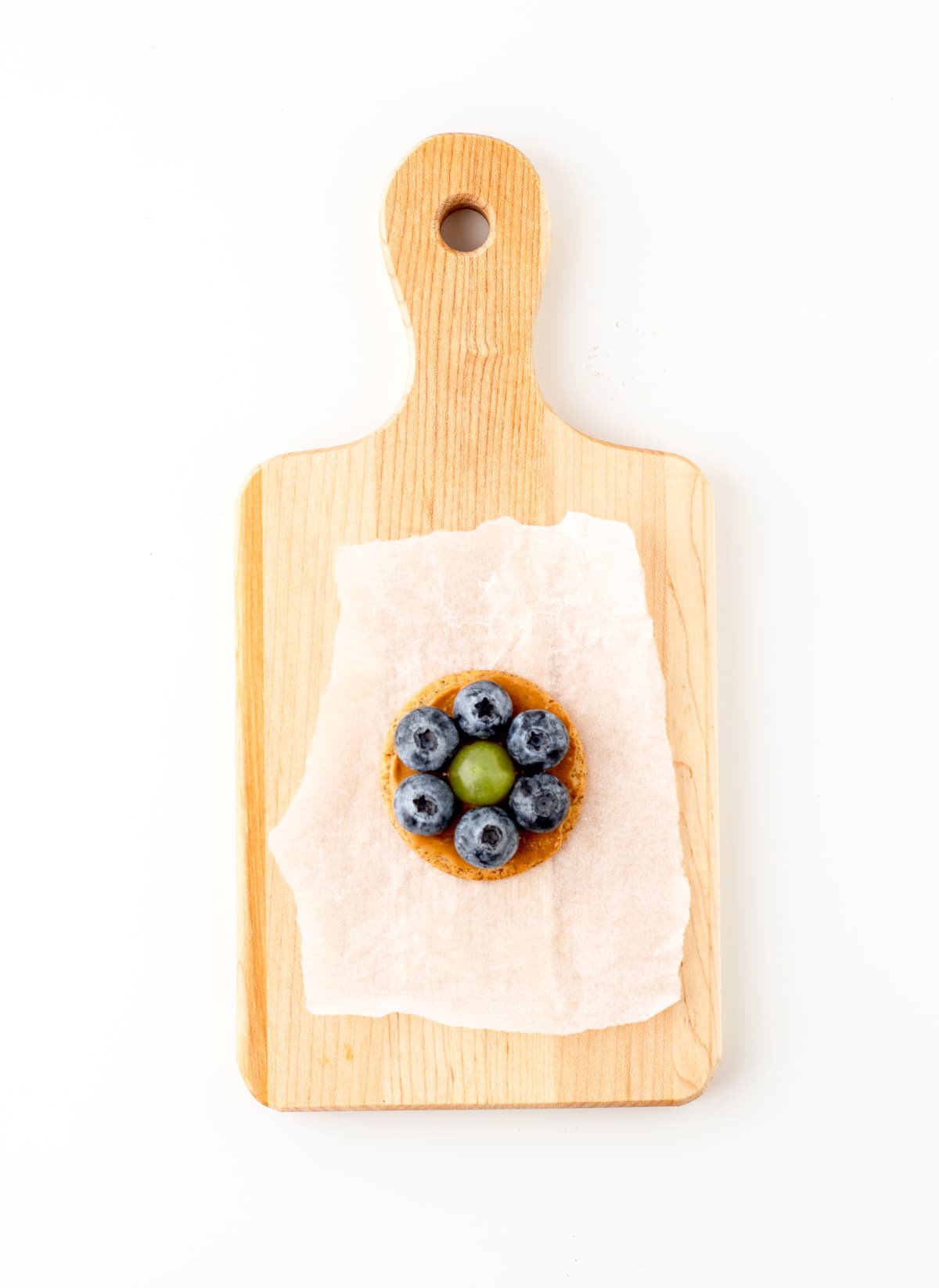 A flower cracker made with blueberries along the perimeter and a grape in the middle on a cutting board.