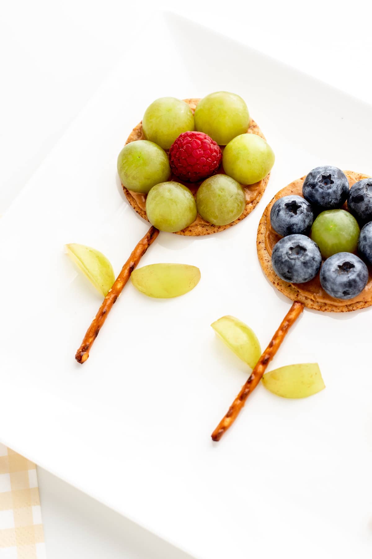 A close-up of two flower crackers on a white platter: one with blueberries along the perimeter, and the other with grapes.