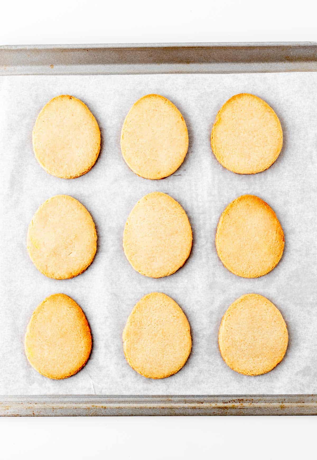 Easter egg-shaped cookies after baking on a baking sheet lined with parchment paper.