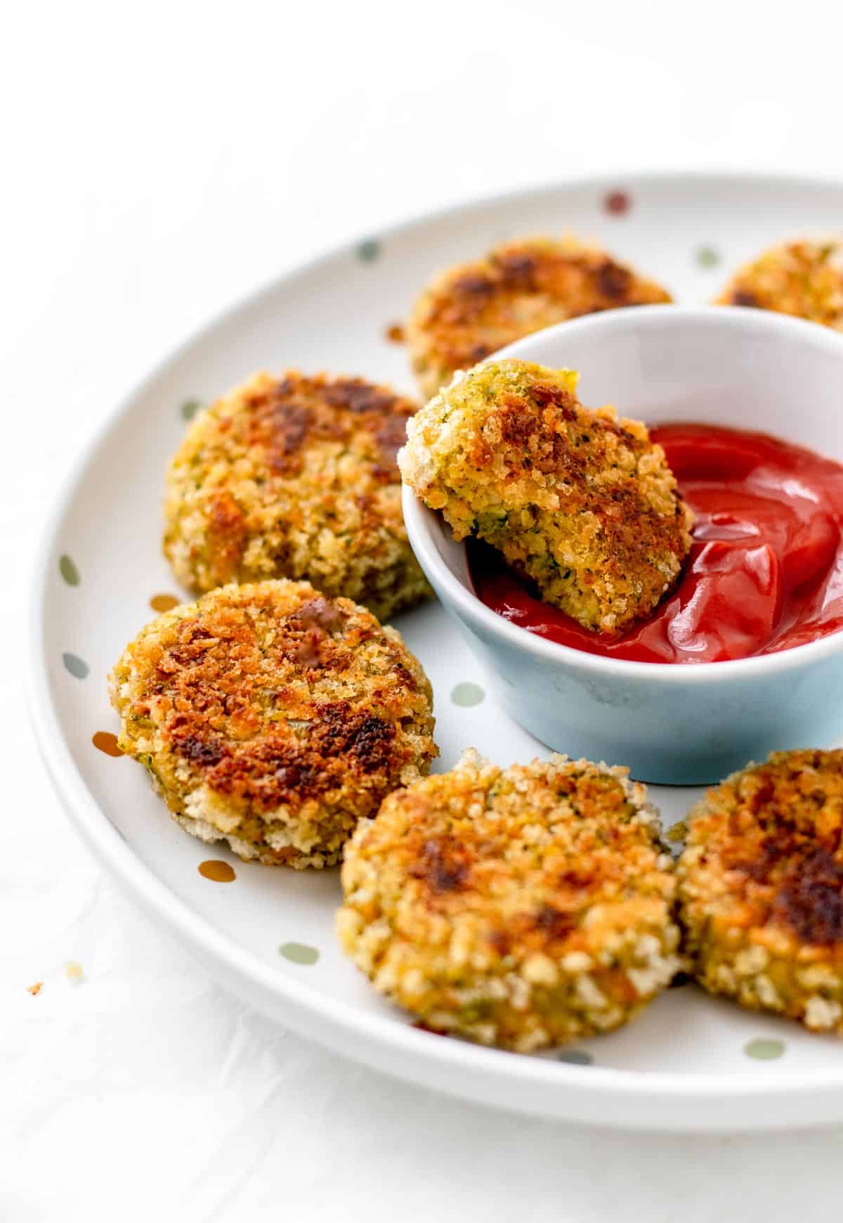 Hidden veggie nuggets on a polka dot plate with one of them being dipped into a bowl of ketchup.